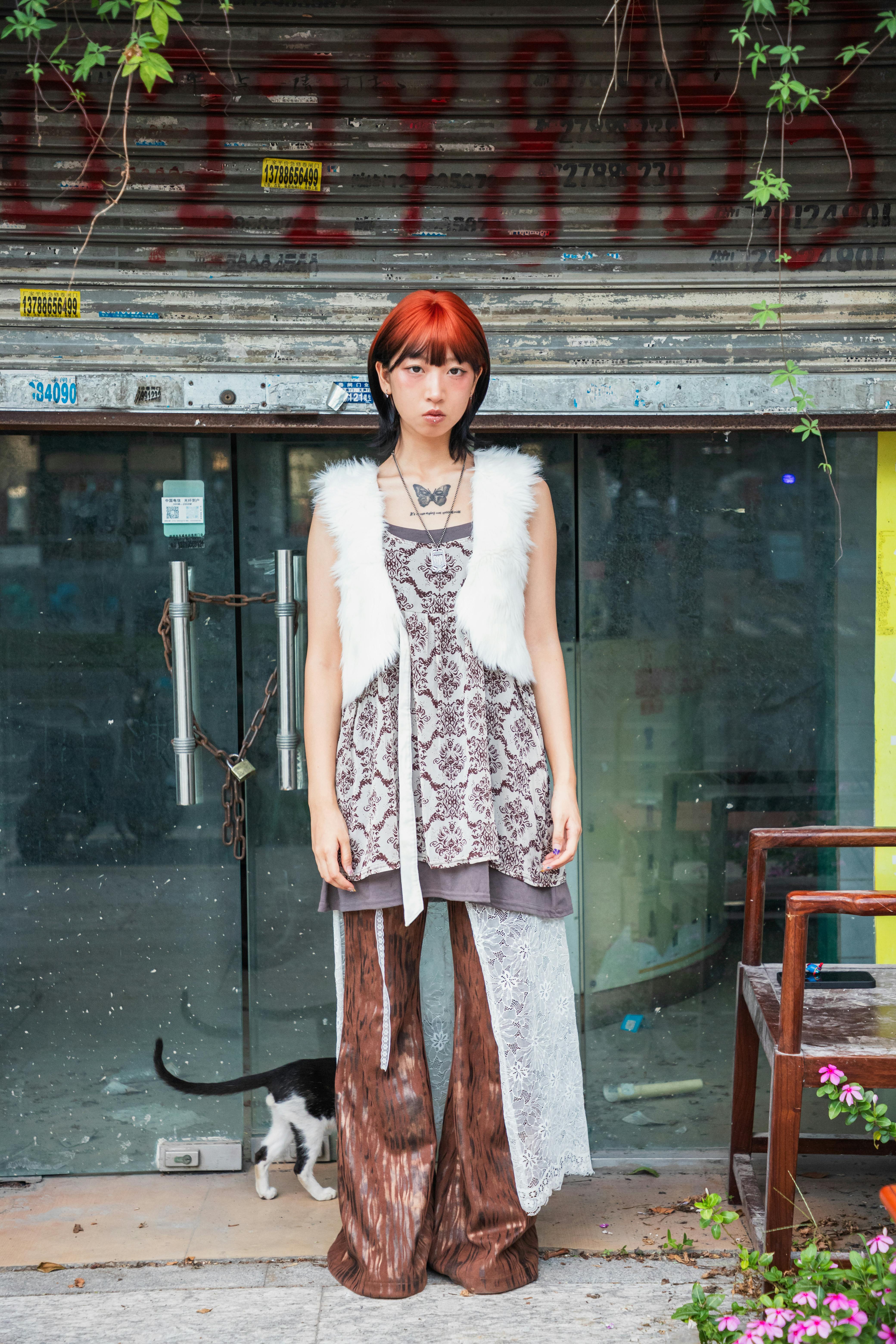 Gratis Una giovane donna elegante, con capelli vivaci e abiti bohémien, è in piedi fuori da un negozio. Foto a disposizione