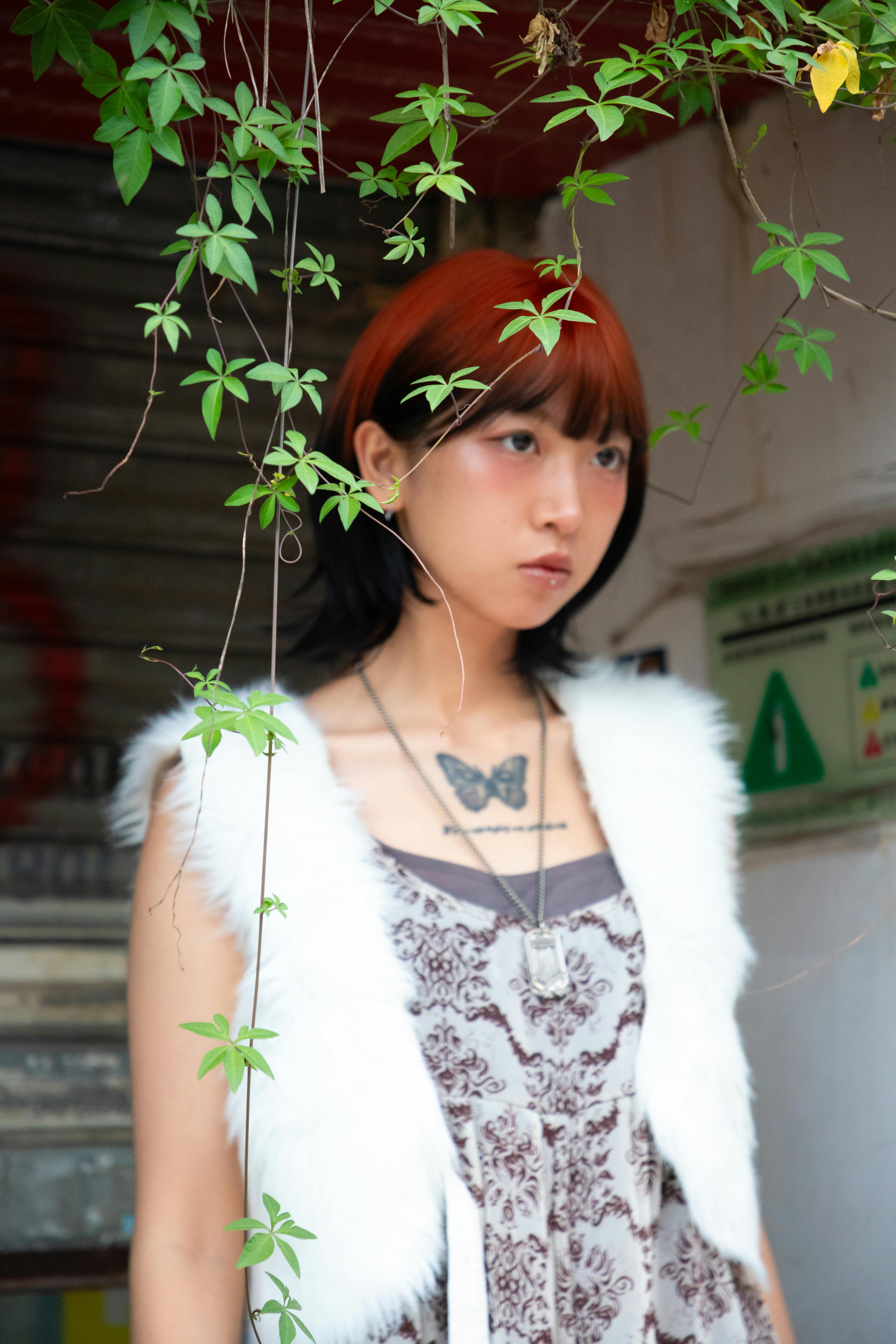 免费 一位时尚年轻女子的肖像，身上有蝴蝶纹身，周围环绕着城市树叶。 素材图片