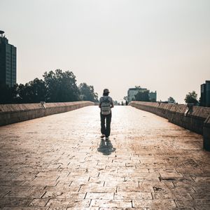 A lone walker on a sunlit stone bridge — photo by Ayşegül Aytören on Pexels