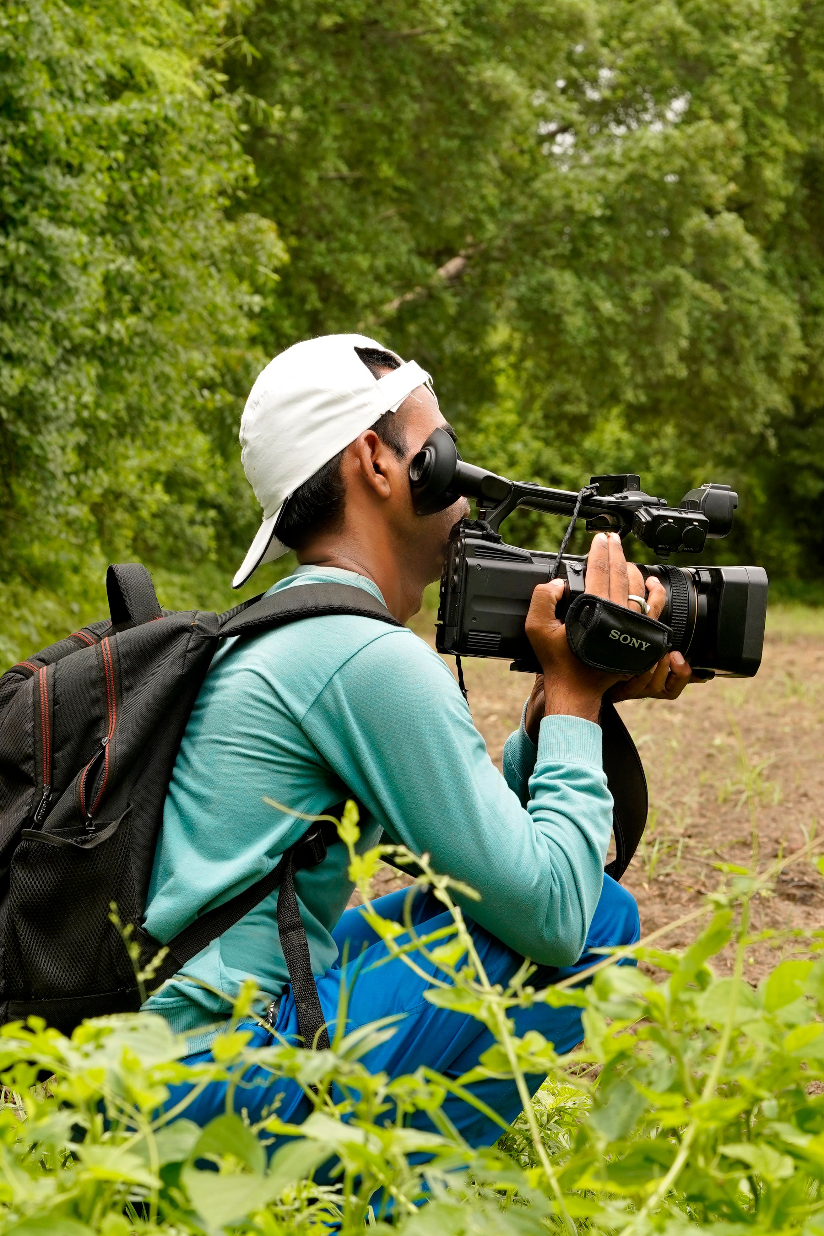 A man films nature outdoors in Sanand, Gujarat, highlighting videography in lush surroundings.
