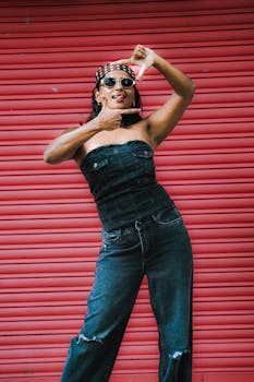 Fashionable woman in denim jumpsuit posing confidently in front of a vibrant red shutter.