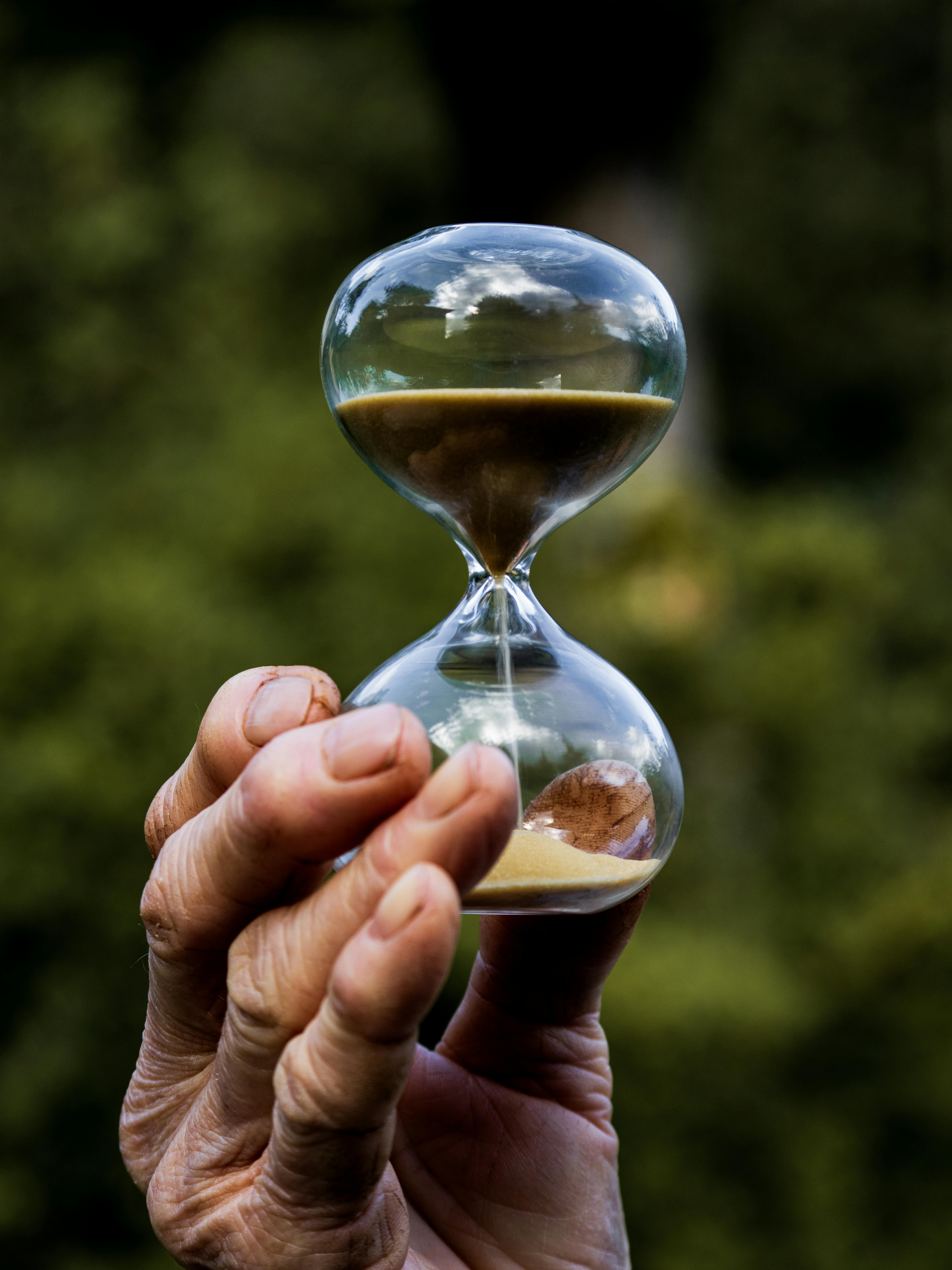 Close-up of an hourglass held by a hand, symbolizing time in a natural setting.