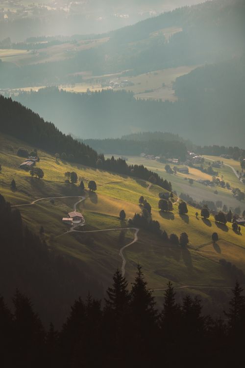 Free A picturesque view of a sunlit alpine valley with winding roads and rolling hills. Stock Photo