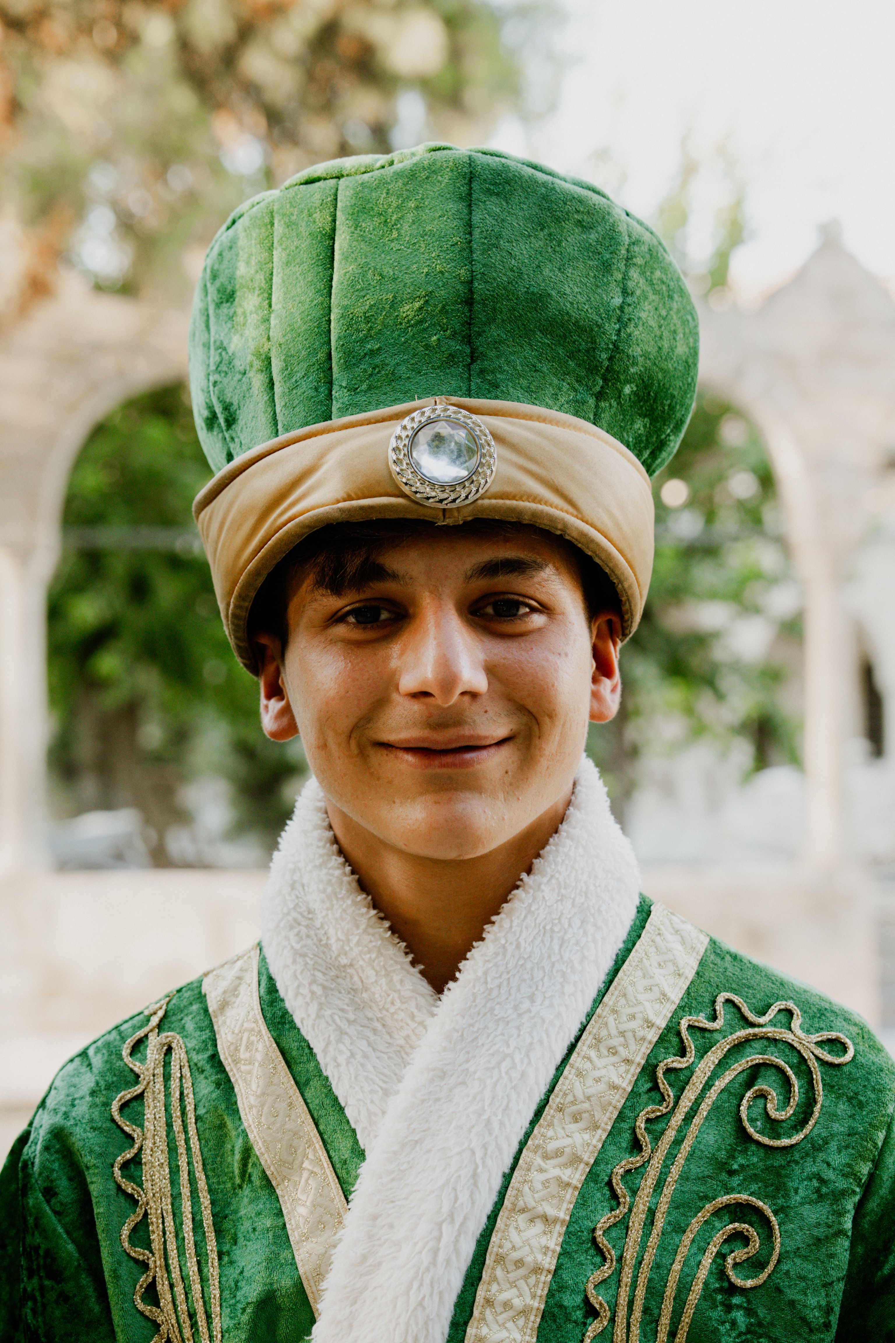 Portrait of a young man in green Ottoman-style attire, smiling outdoors.