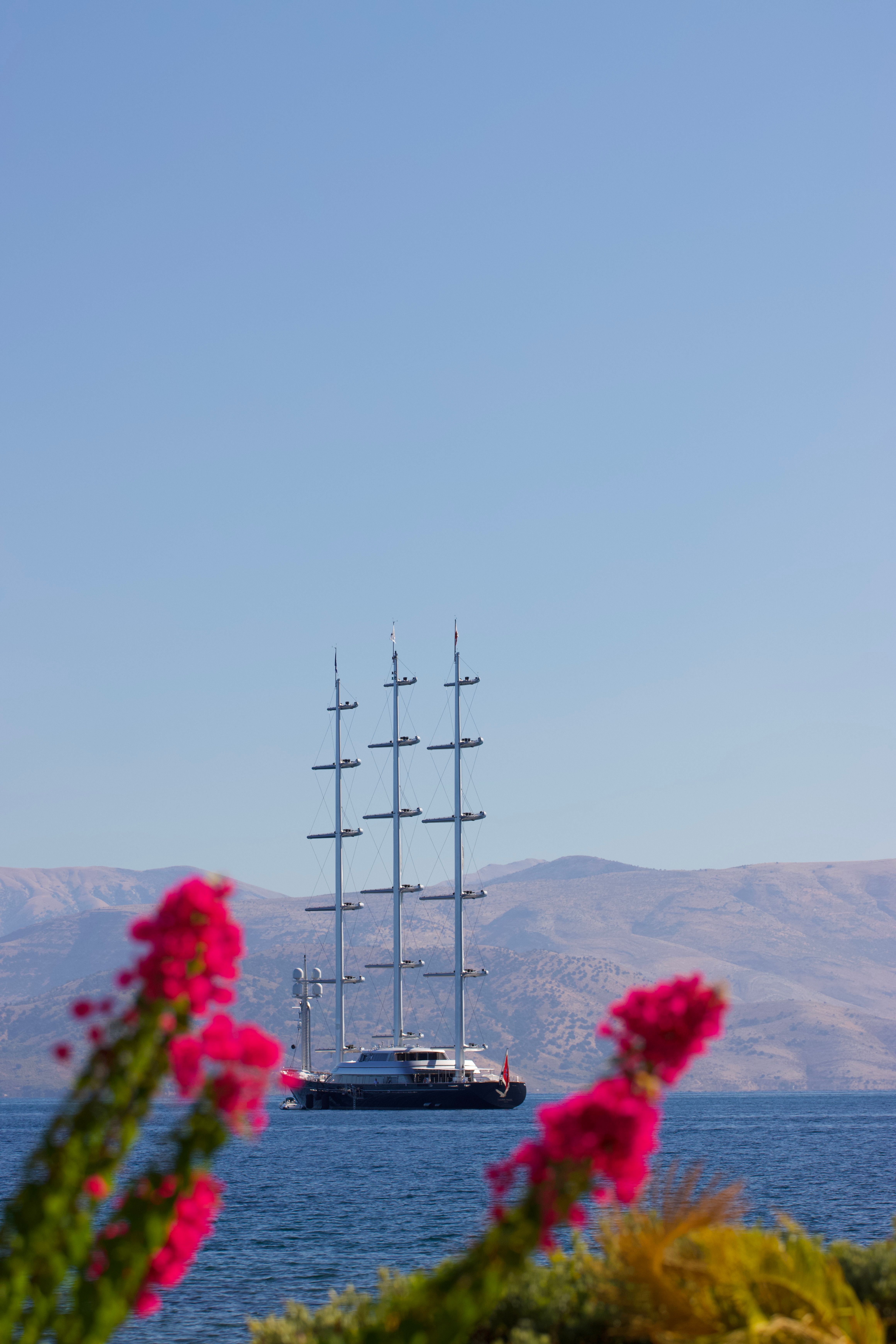 Stunning view of a luxury yacht sailing in Corfu, Greece with vibrant pink flowers in the foreground.