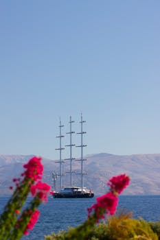 Stunning view of a luxury yacht sailing in Corfu, Greece with vibrant pink flowers in the foreground.