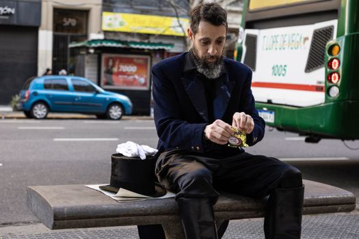 Un signore in abiti d'epoca è seduto su una panchina a Buenos Aires, in Argentina, mentre scarta una caramella.
