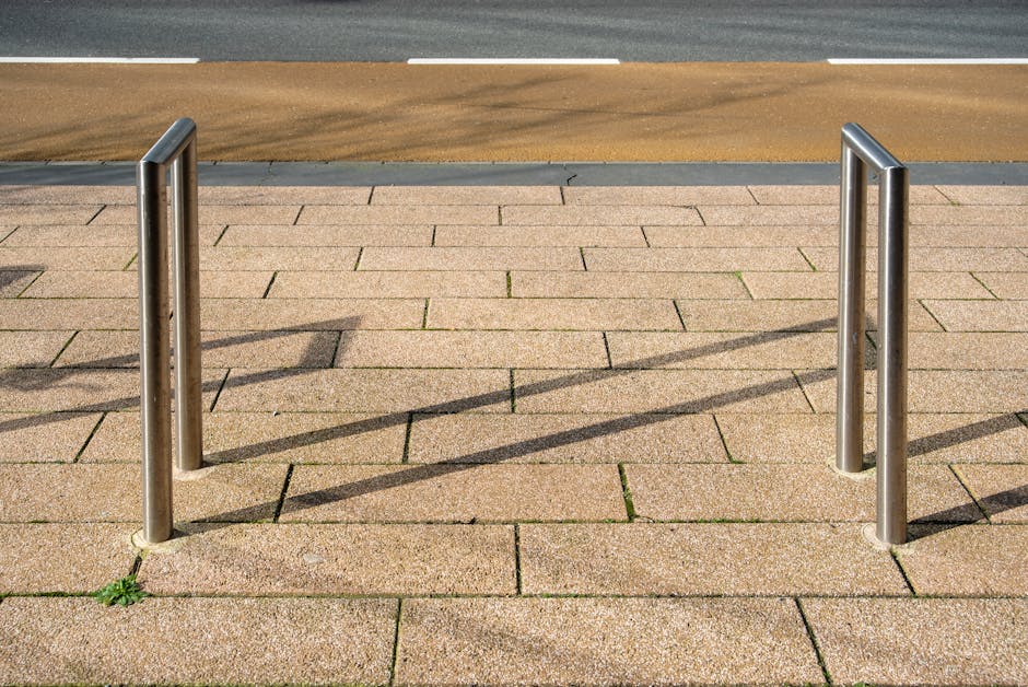A clean, empty bicycle stand on a textured paved sidewalk with shadows, street in sight.