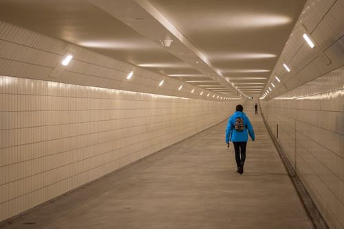 Free Person in blue jacket walking through a well-lit underground tunnel in Rotterdam. Stock Photo