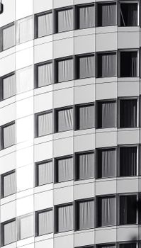 Architectural close-up of a modern, curved building facade with multiple windows in black and white.