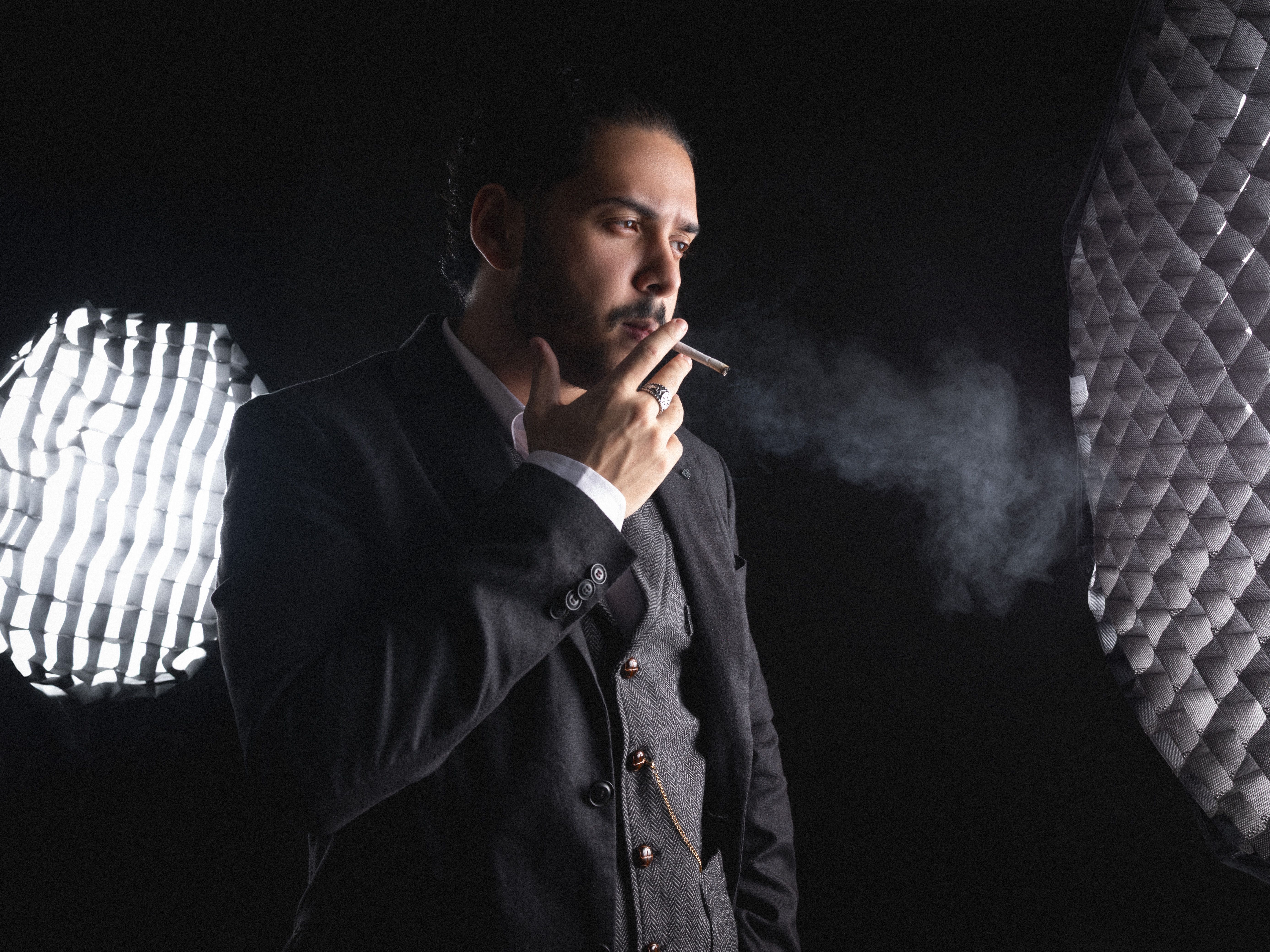 Portrait of a well-dressed man smoking a cigar in a professional studio setting with dramatic lighting.