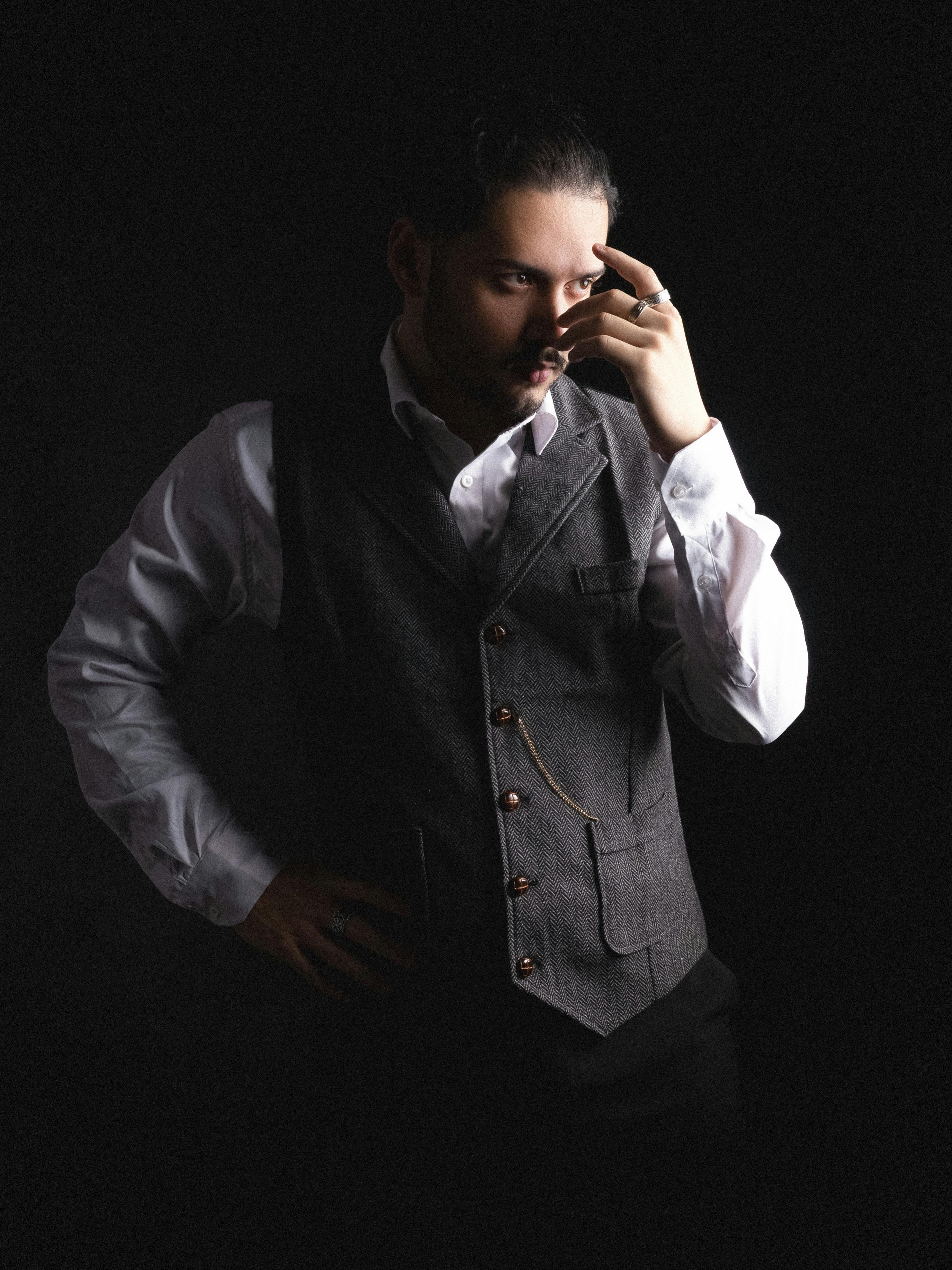 Free Sophisticated man in a dark vest poses with hand on face, set against a moody backdrop. Stock Photo