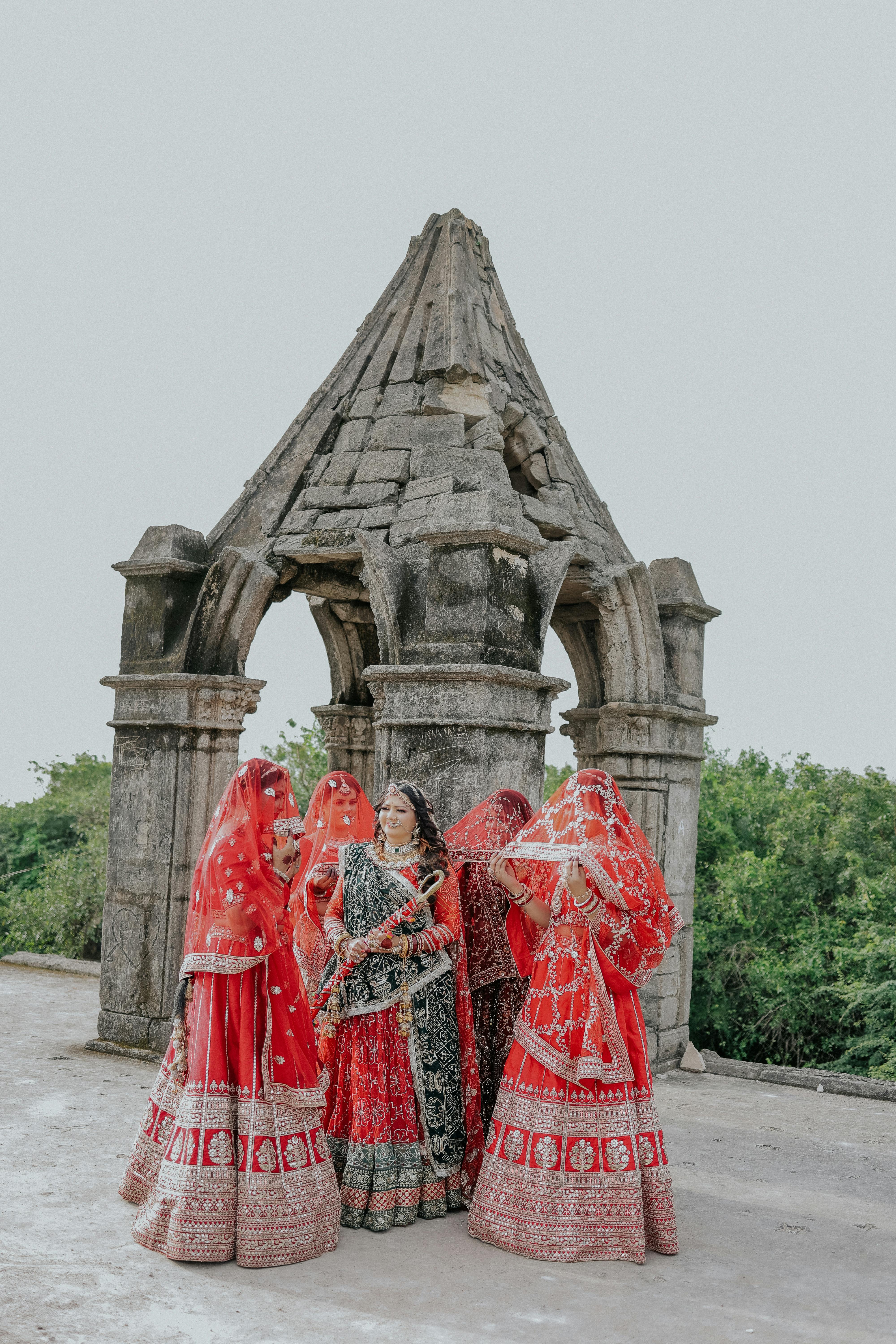 Indian women in vibrant wedding attire celebrating outdoors at a historical site.