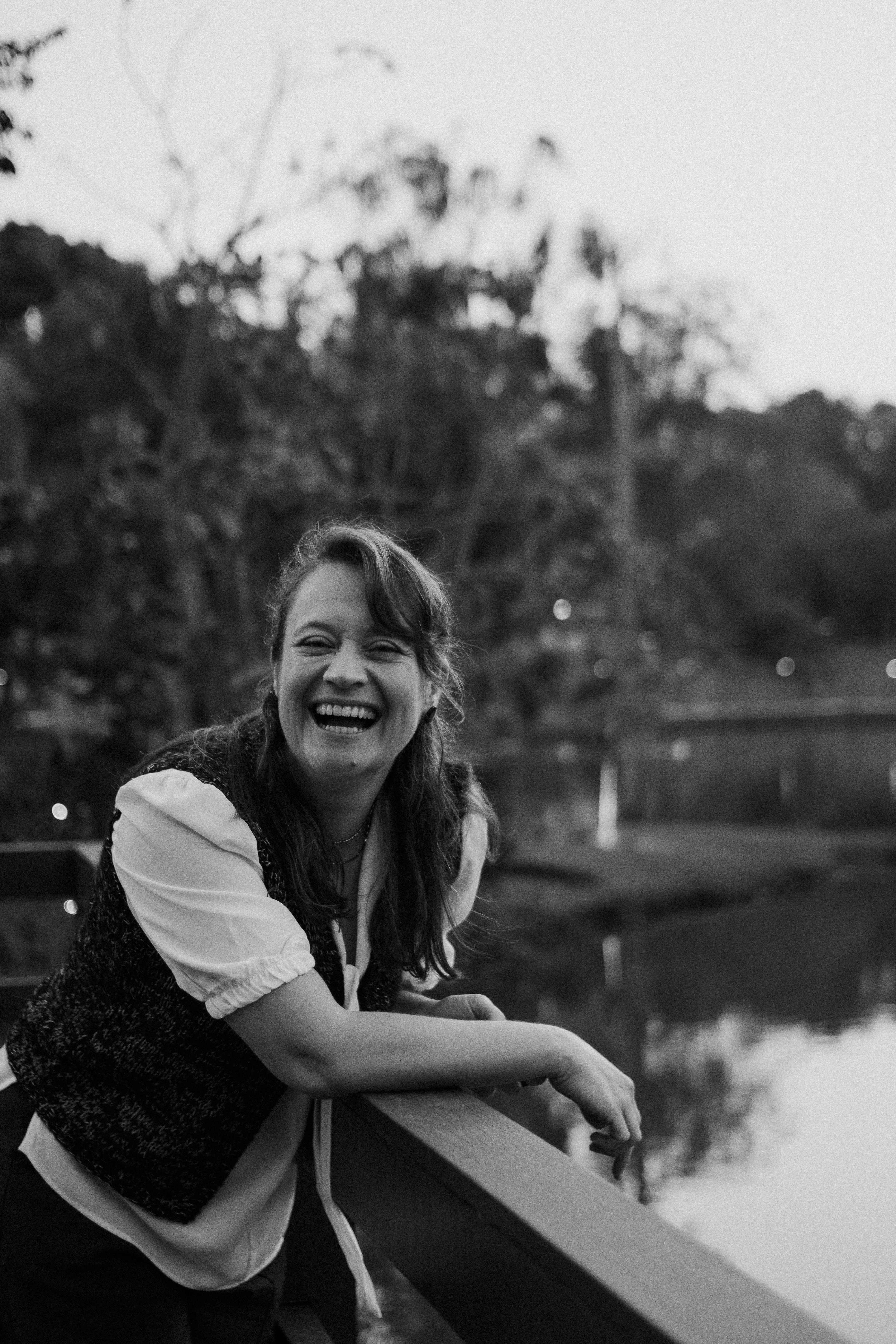 Black and white photo of a joyful woman laughing by a lake in a park.
