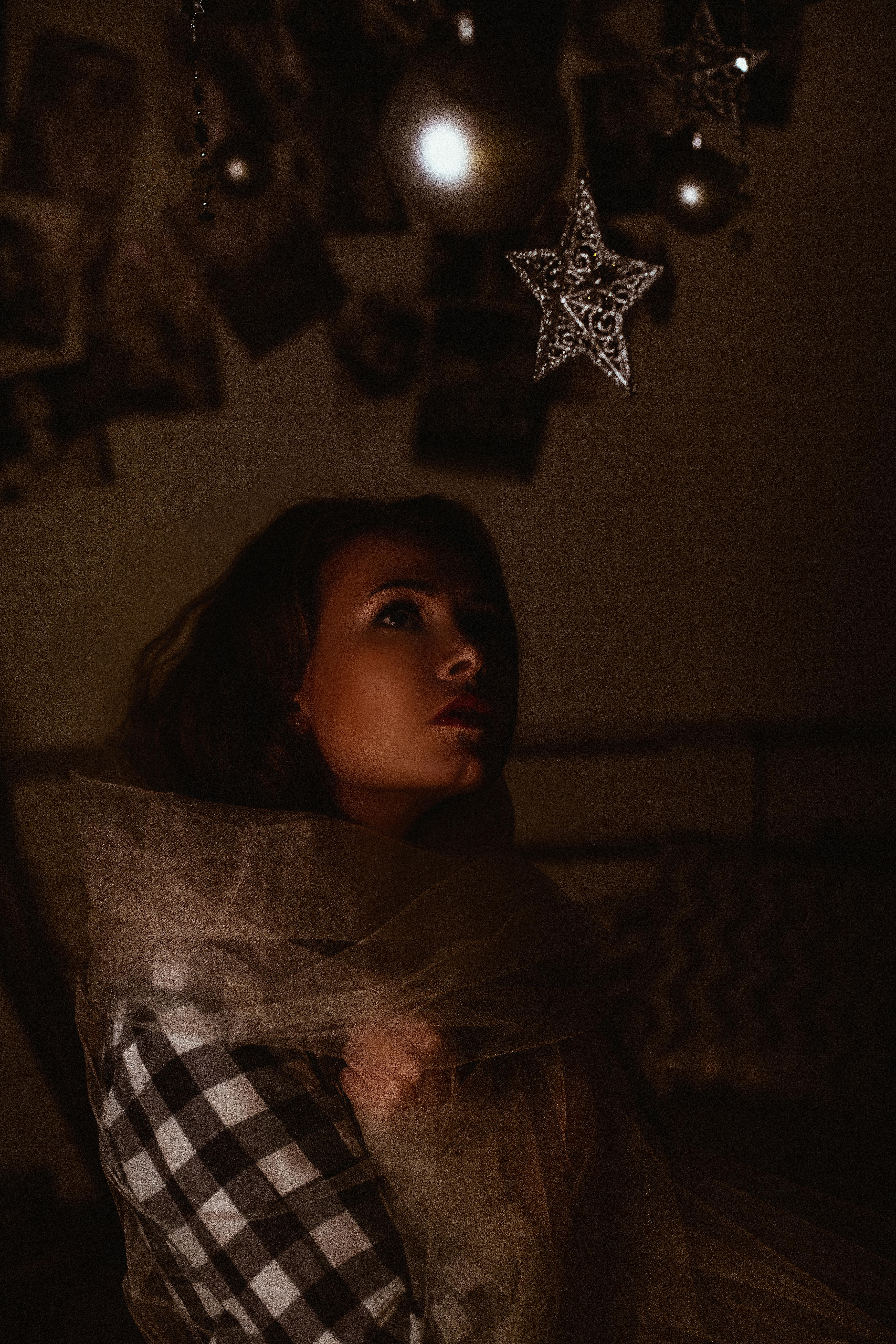 在光线昏暗的房间里，一名女子裹着柔软的织物，凝视着悬挂的明星装饰