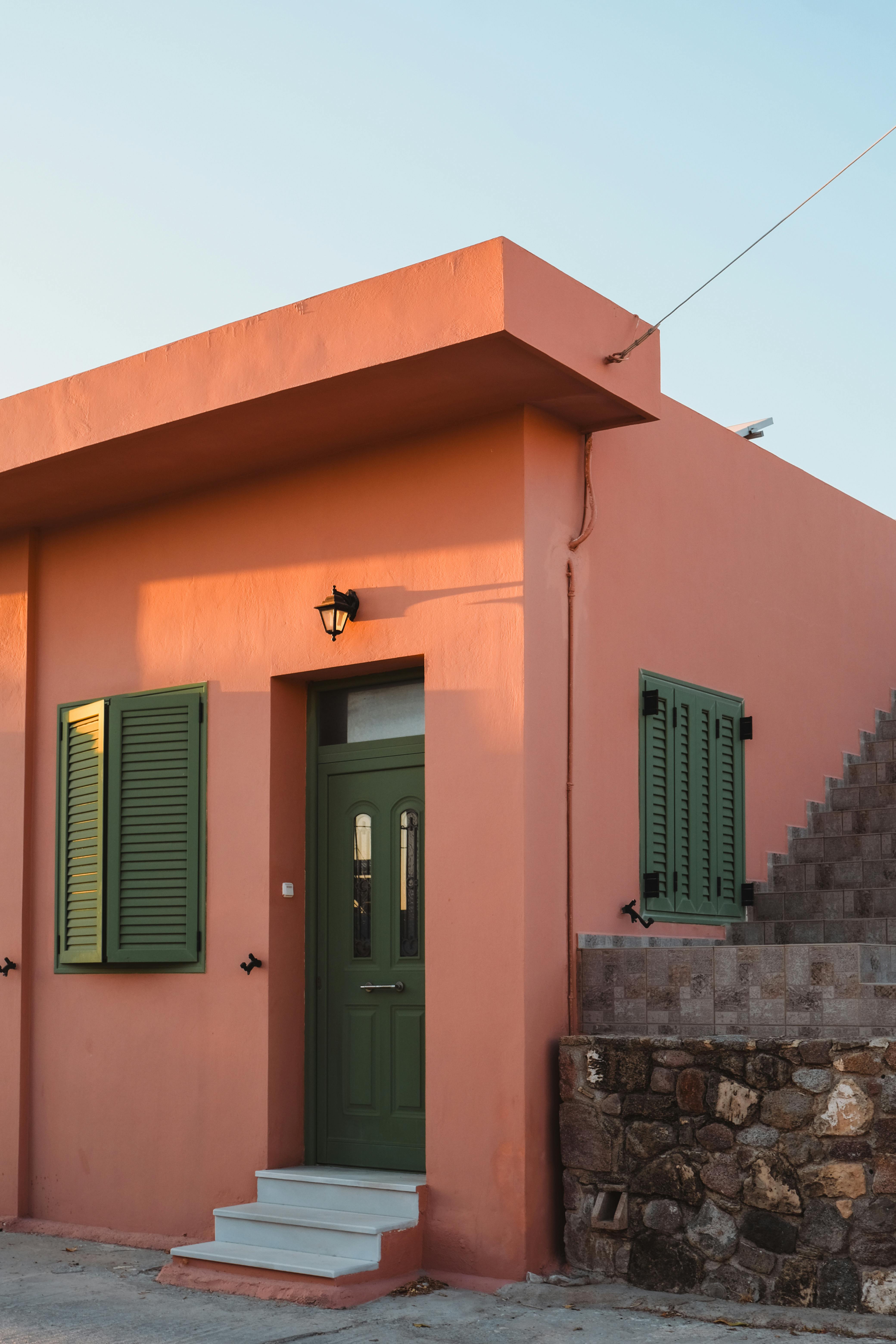 Sunlit Mediterranean house facade with green shutters at golden hour, capturing a warm, inviting atmosphere.