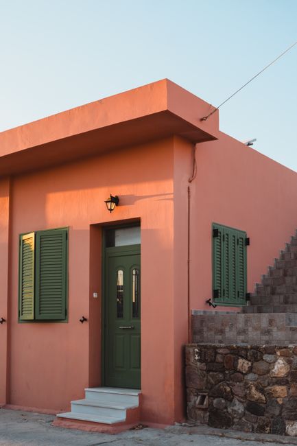 Sunlit Mediterranean house facade with green shutters at golden hour, capturing a warm, inviting atmosphere.