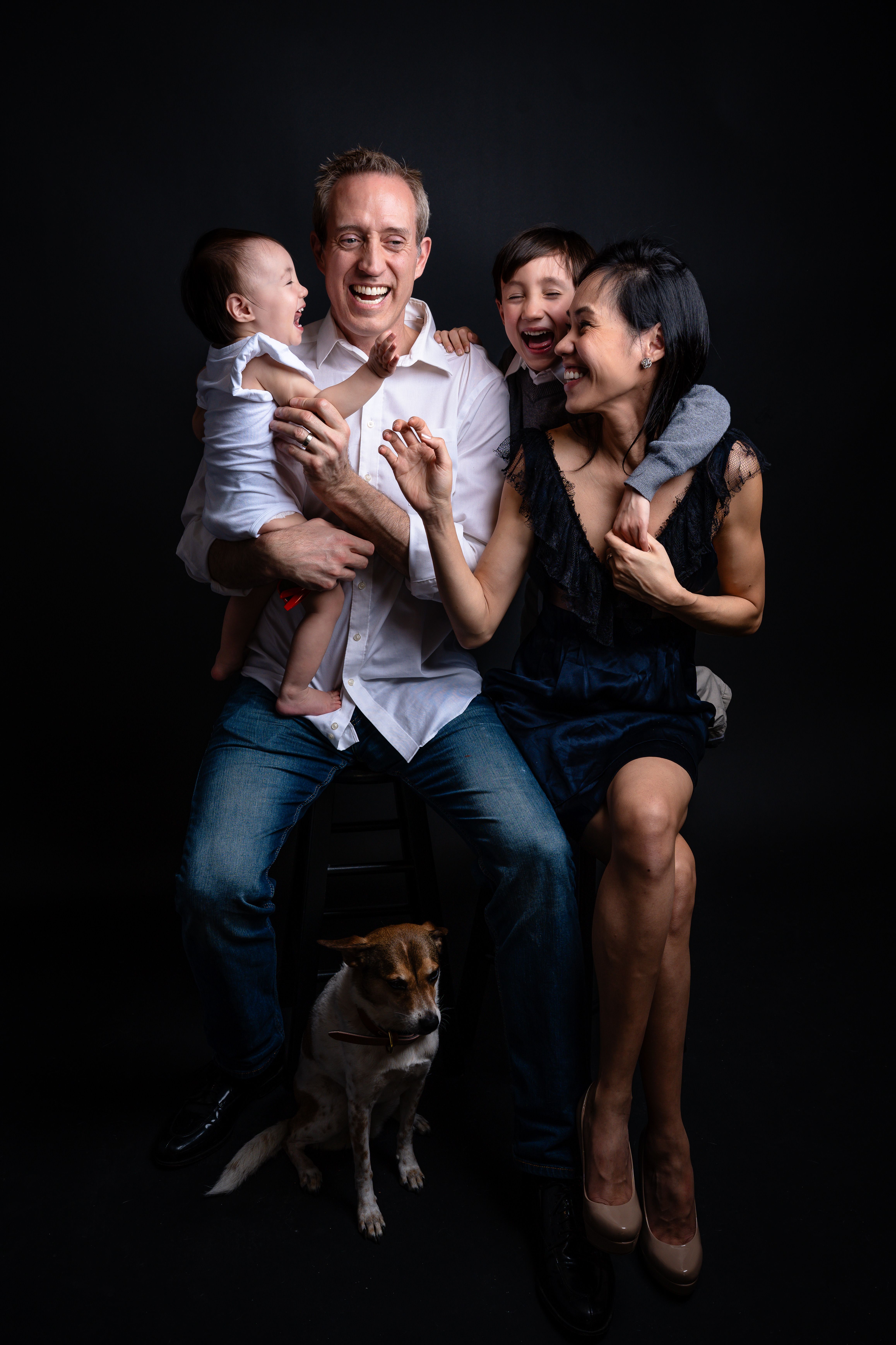 Happy family with two children and dog in a studio setting, laughing and playing.
