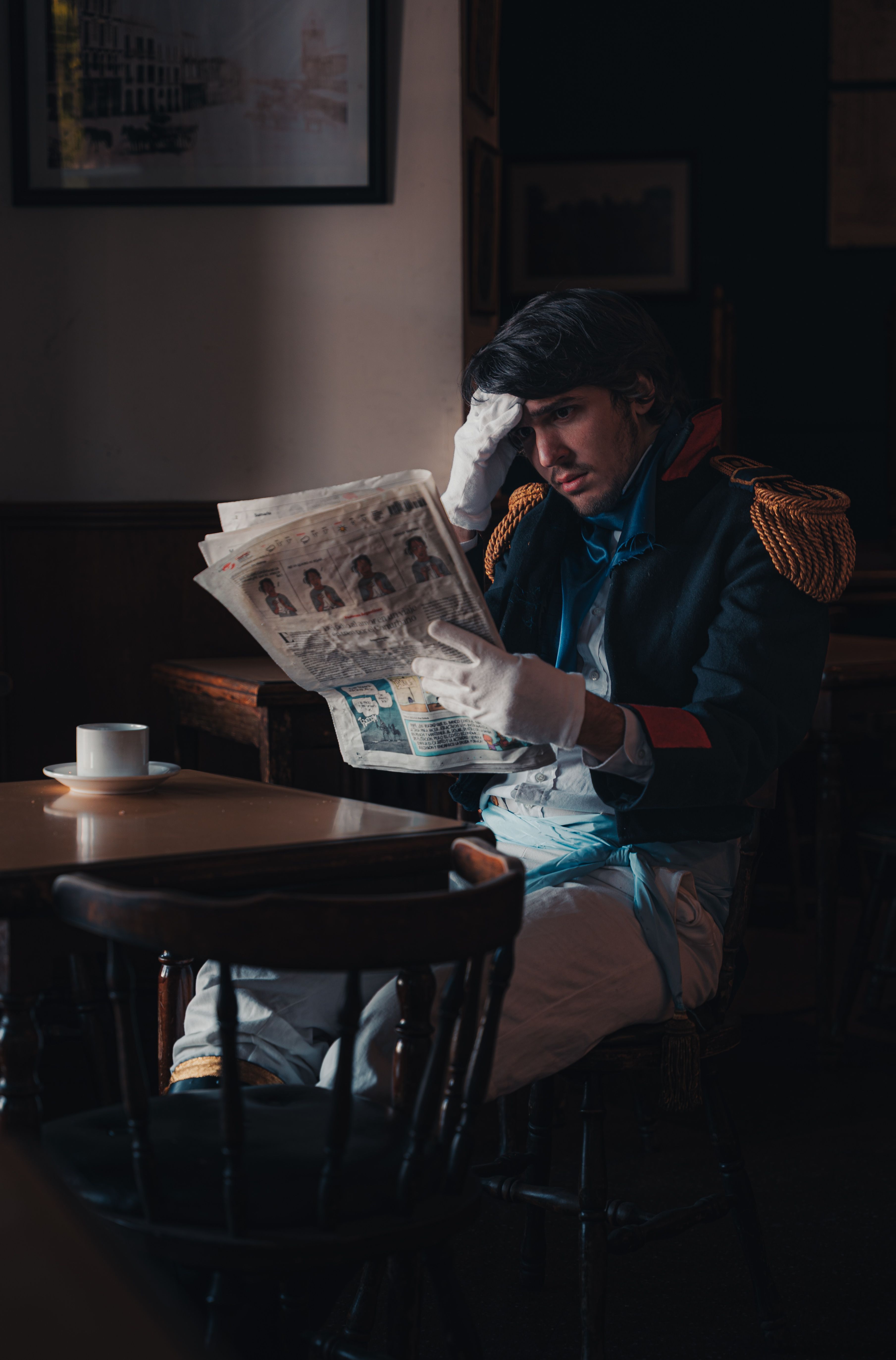 Man in historical military attire reading a newspaper in a dimly lit cafe.
