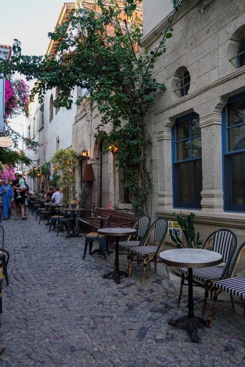 Free Idyllic cobblestone alley with outdoor cafés enveloped in greenery and flowers. Stock Photo