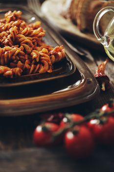 Close-up of fusilli pasta on a rustic table with cherry tomatoes and olive oil.