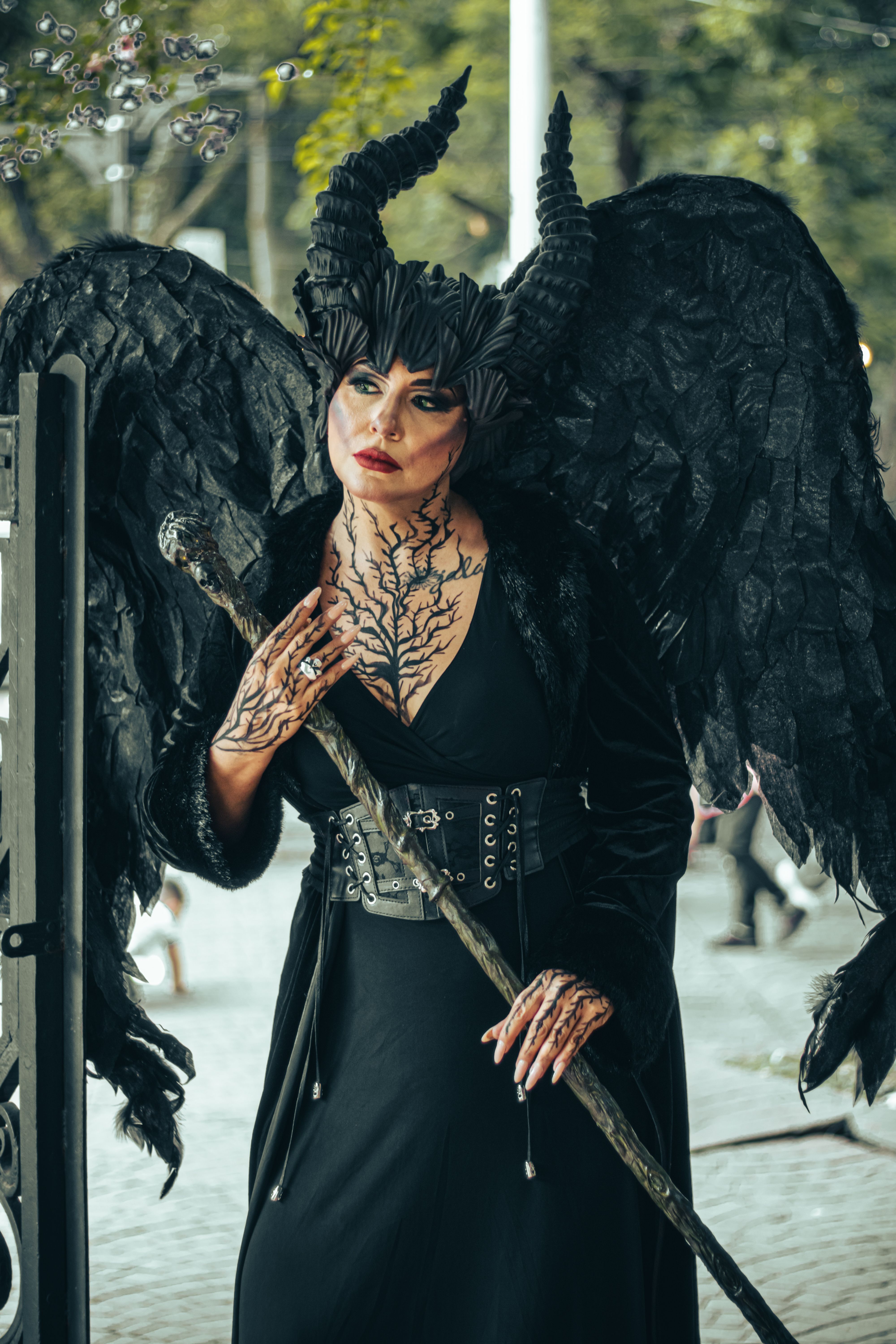 Mystical being in gothic attire with horns and black wings standing in an urban setting.