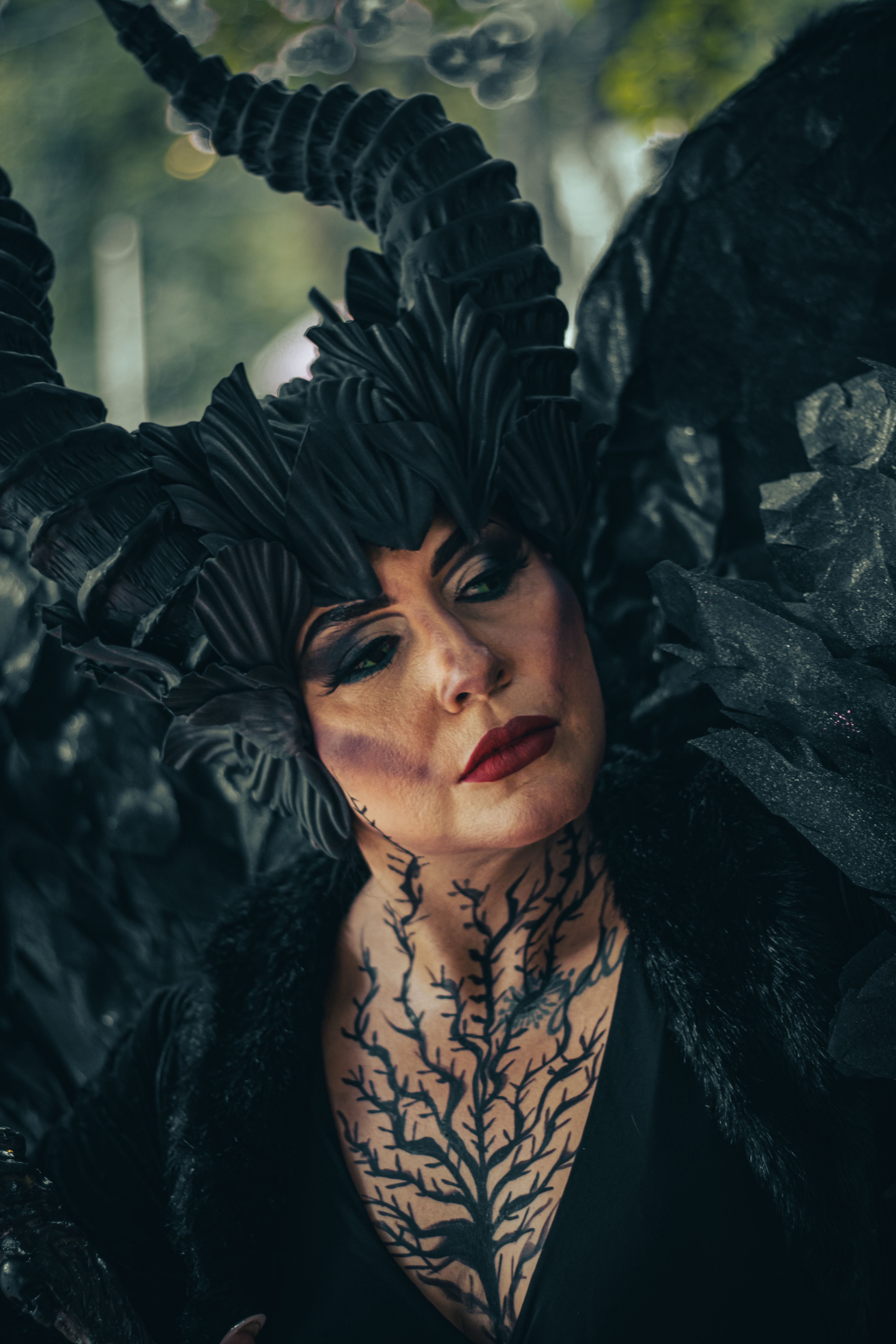 A striking dark fantasy costume with elaborate horns and wings in an artistic makeup look.