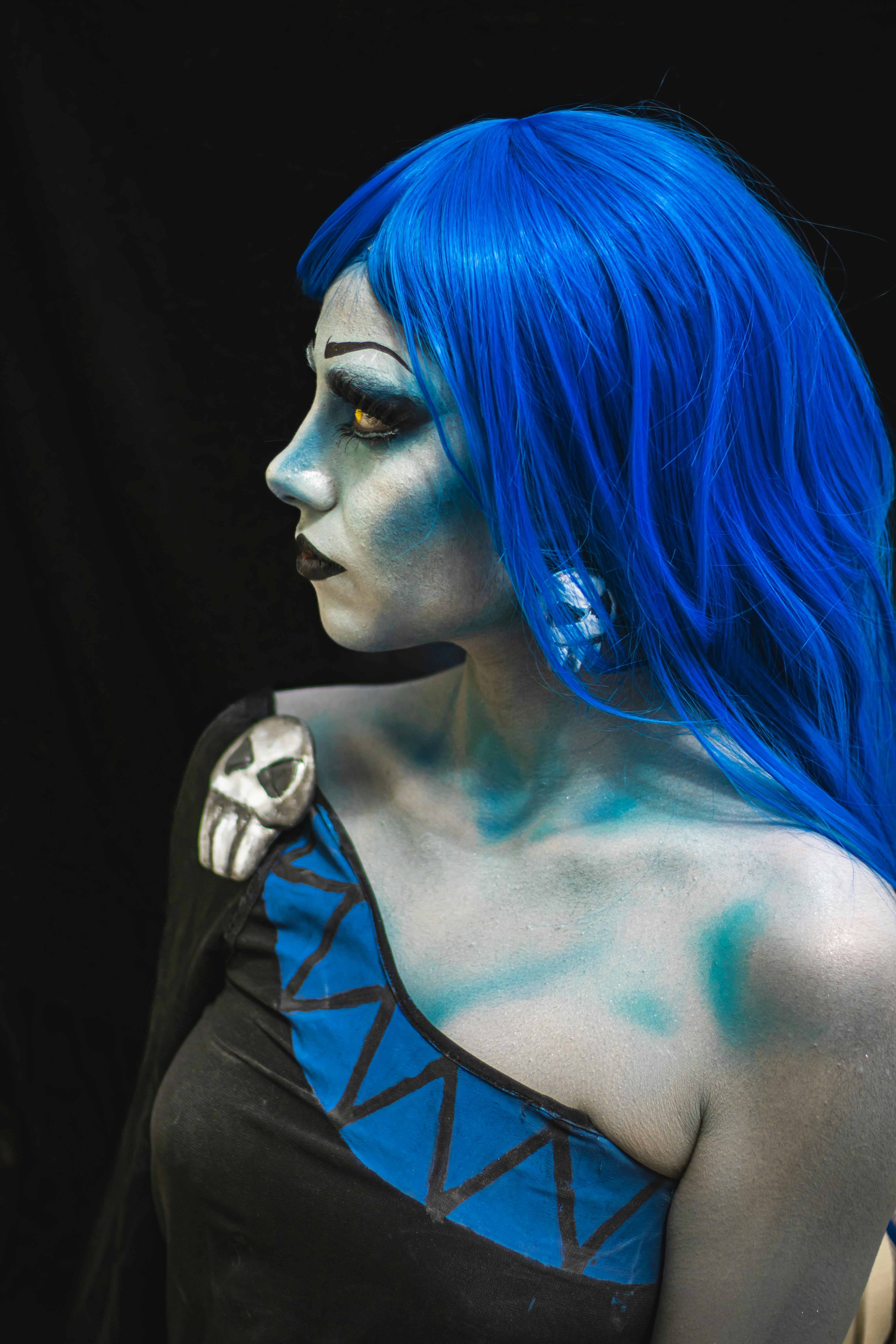 Ücretsiz Yaratıcı mavi makyajlı ve canlı mavi saçlı, koyu bir arka plana karşı cosplay yapan bir kadının yan profili. Stok Fotoğraflar