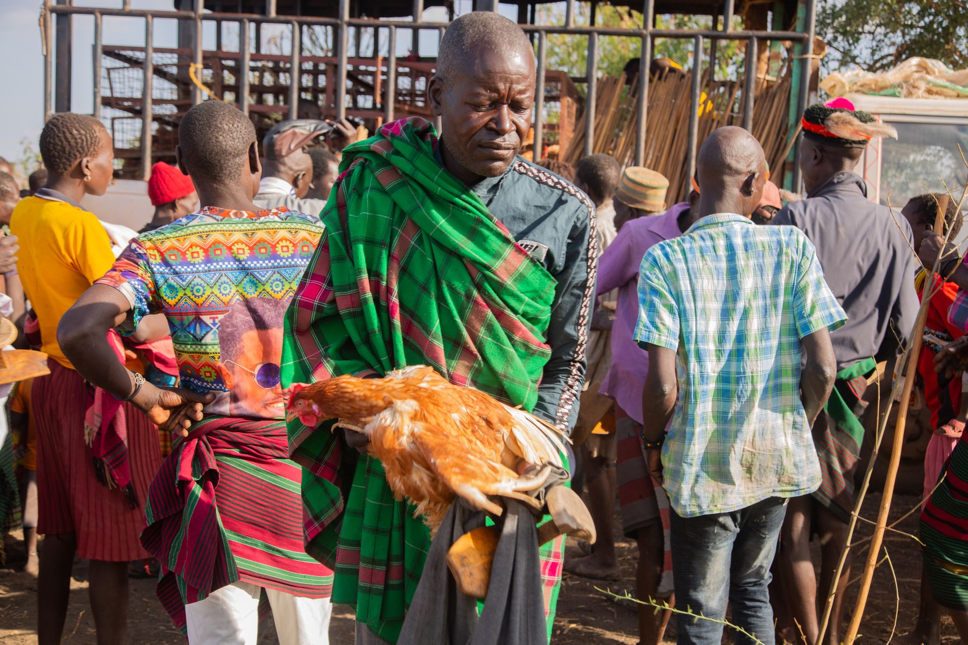 Tribal market scene with vibrant clothing and chicken in hand, showcasing traditional trade.