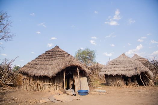 Rural African village with traditional grass huts under a clear blue sky.
