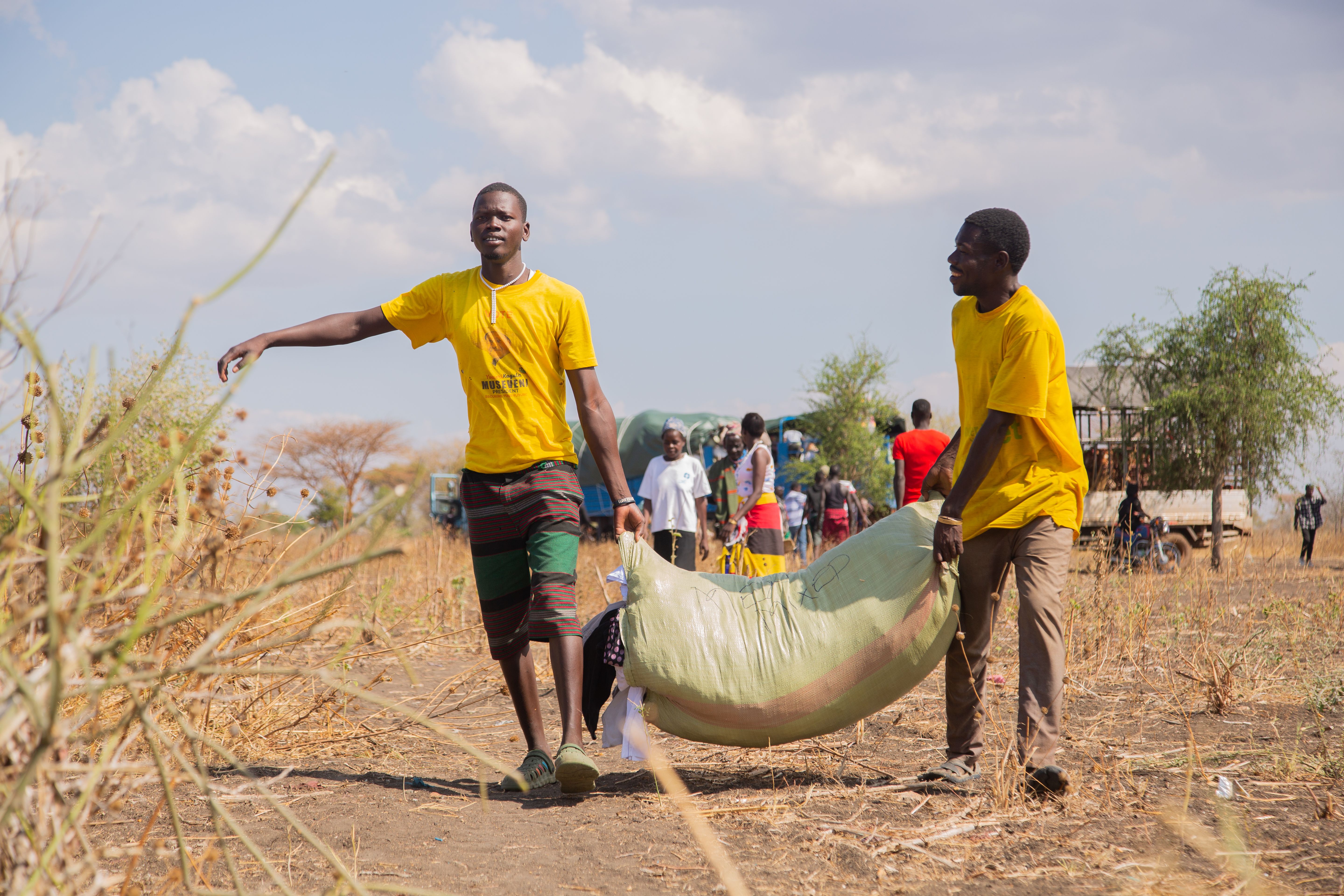 Volunteers in yellow shirts transport aid supplies in a rural landscape, highlighting community assistance.