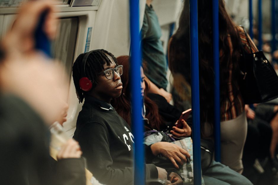 Diverse commuters on a busy London Underground train, one wearing headphones.
