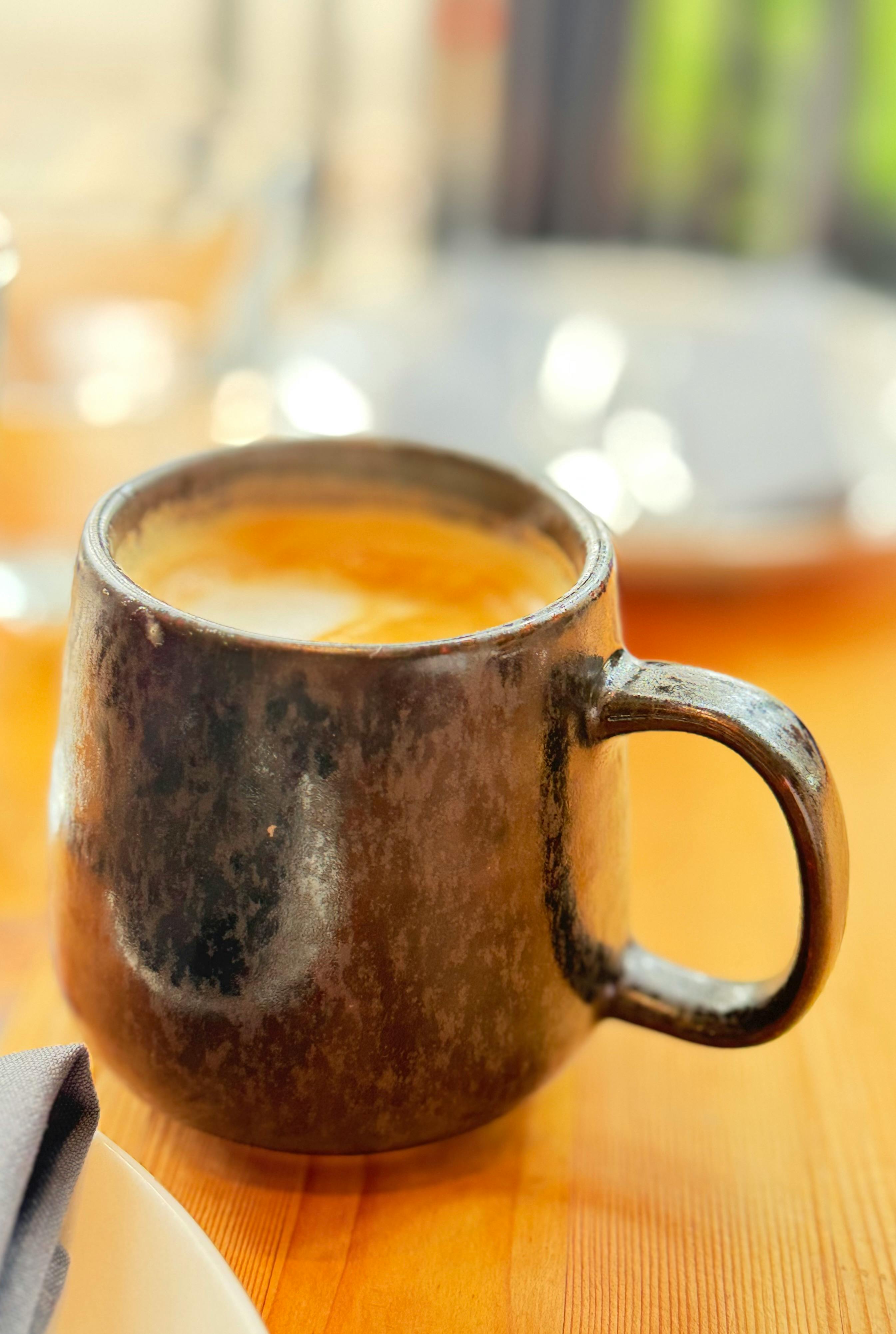 Close-up of a rustic ceramic mug filled with a creamy latte on a wooden table.