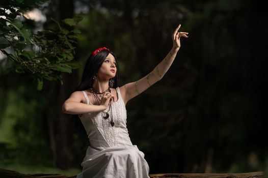 A woman in a white dress reaches gracefully in a serene forest setting, creating a mystical ambiance.