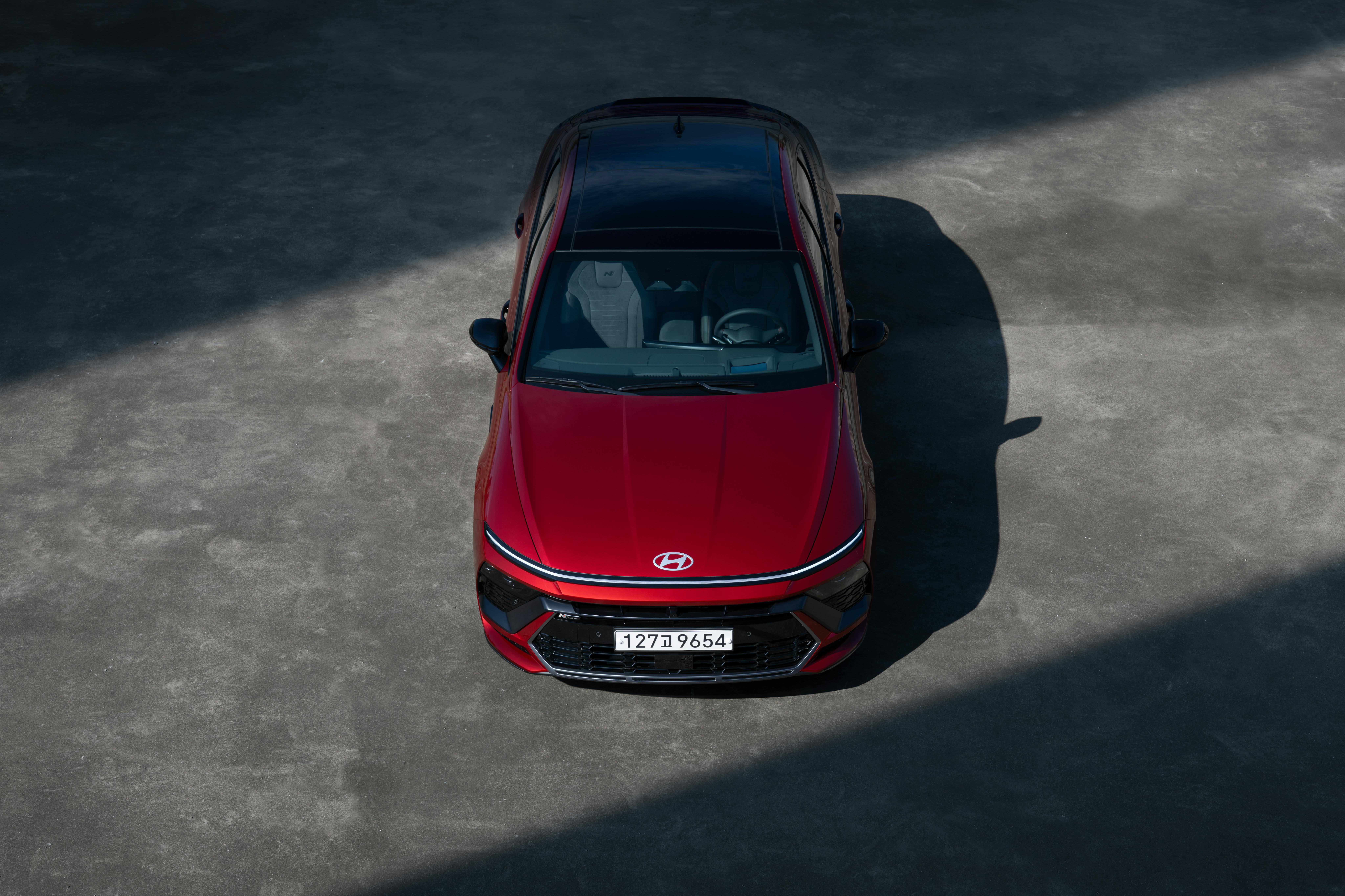 A sleek red Hyundai sedan in an outdoor parking area, viewed from above with dramatic shadowing.