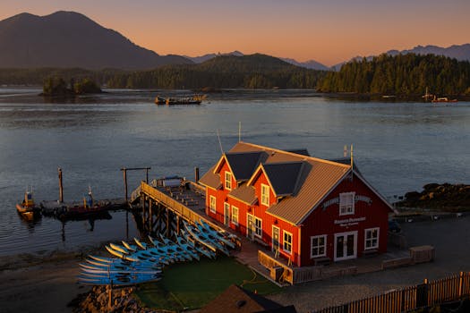 A picturesque scene of Tofino Harbor during sunset featuring red building and kayaks.