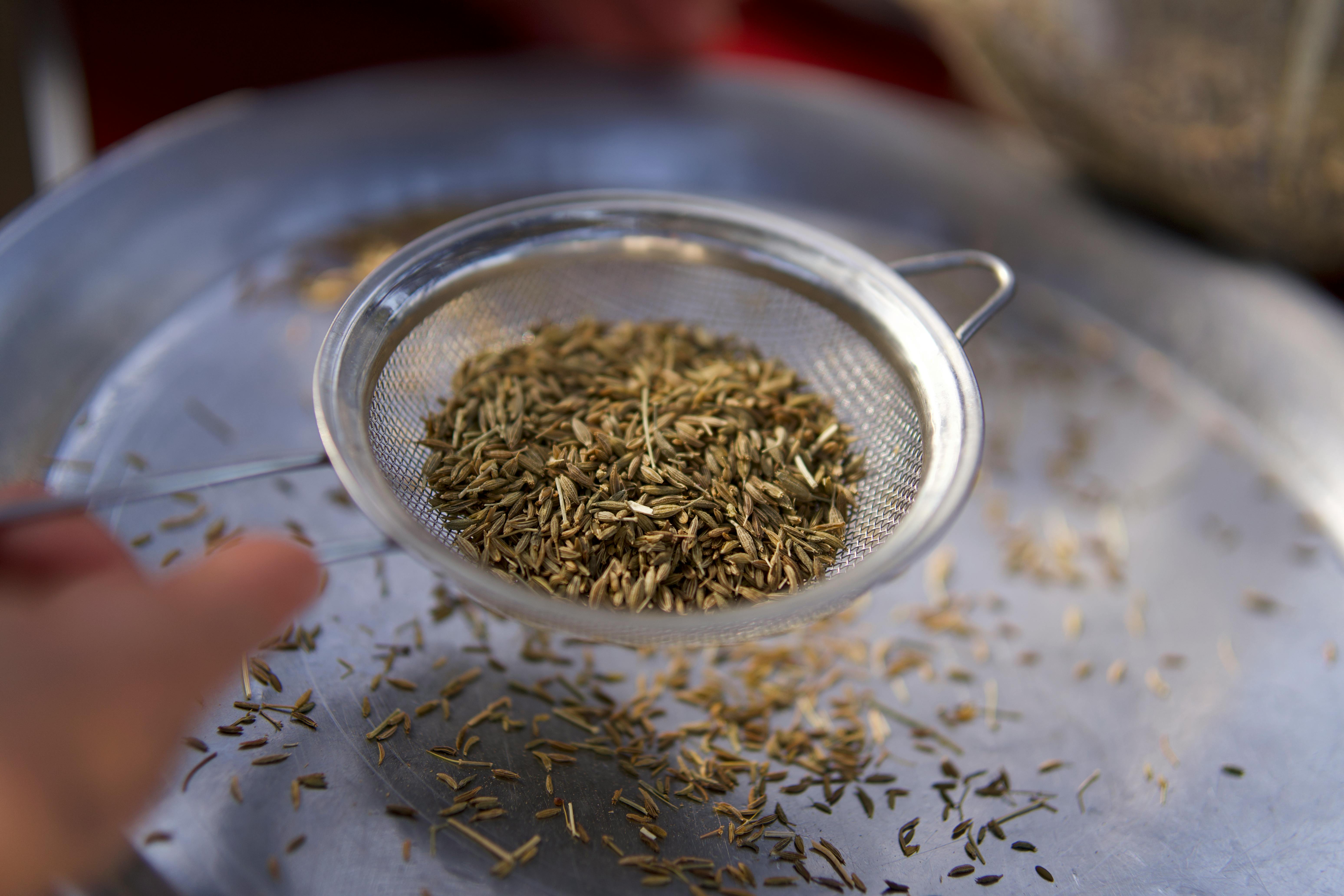 Close-up of sieve filtering cumin seeds over a metal tray, highlighting culinary preparation.