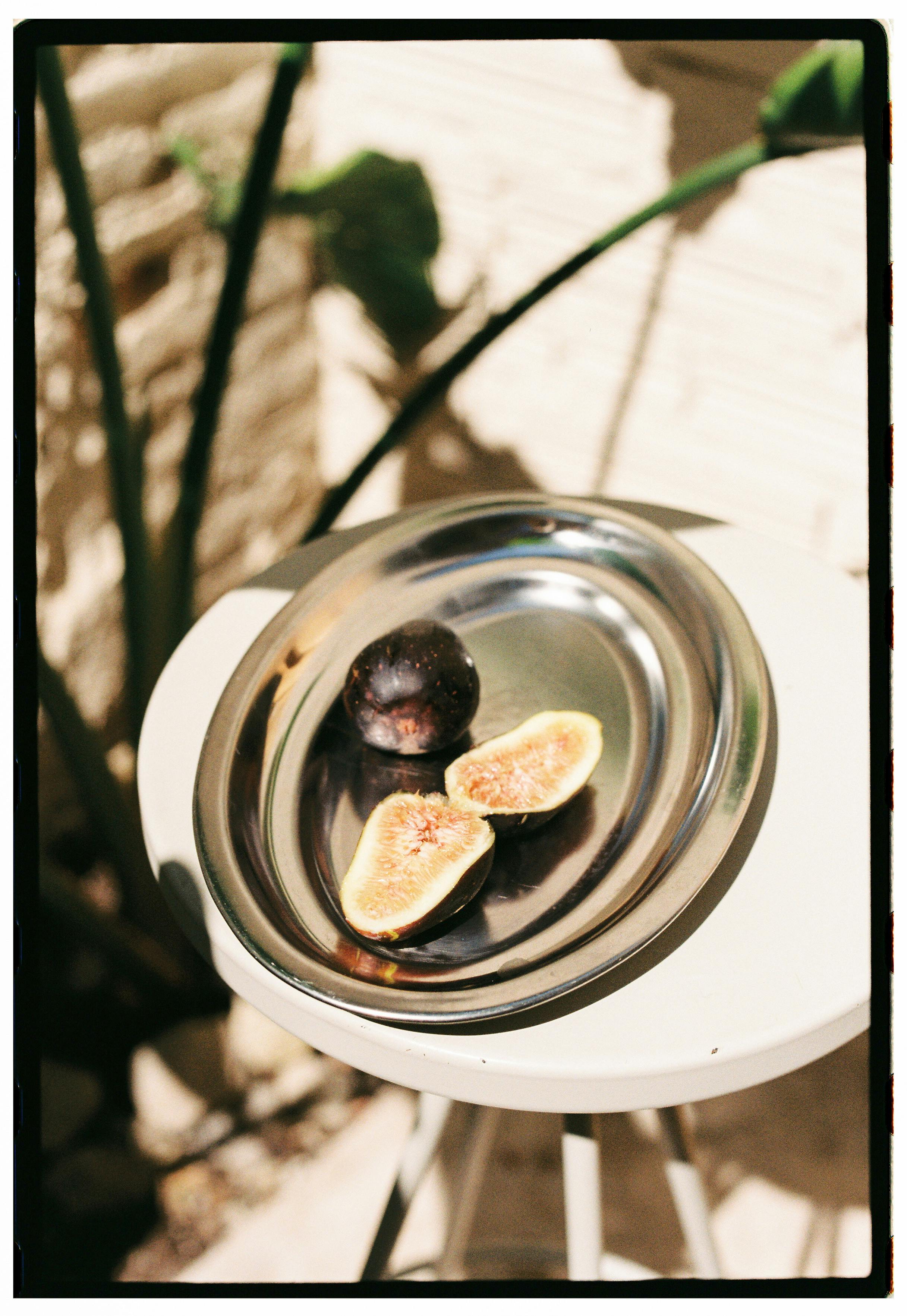 Close-up of fresh figs, whole and halved, on a silver tray outdoors.