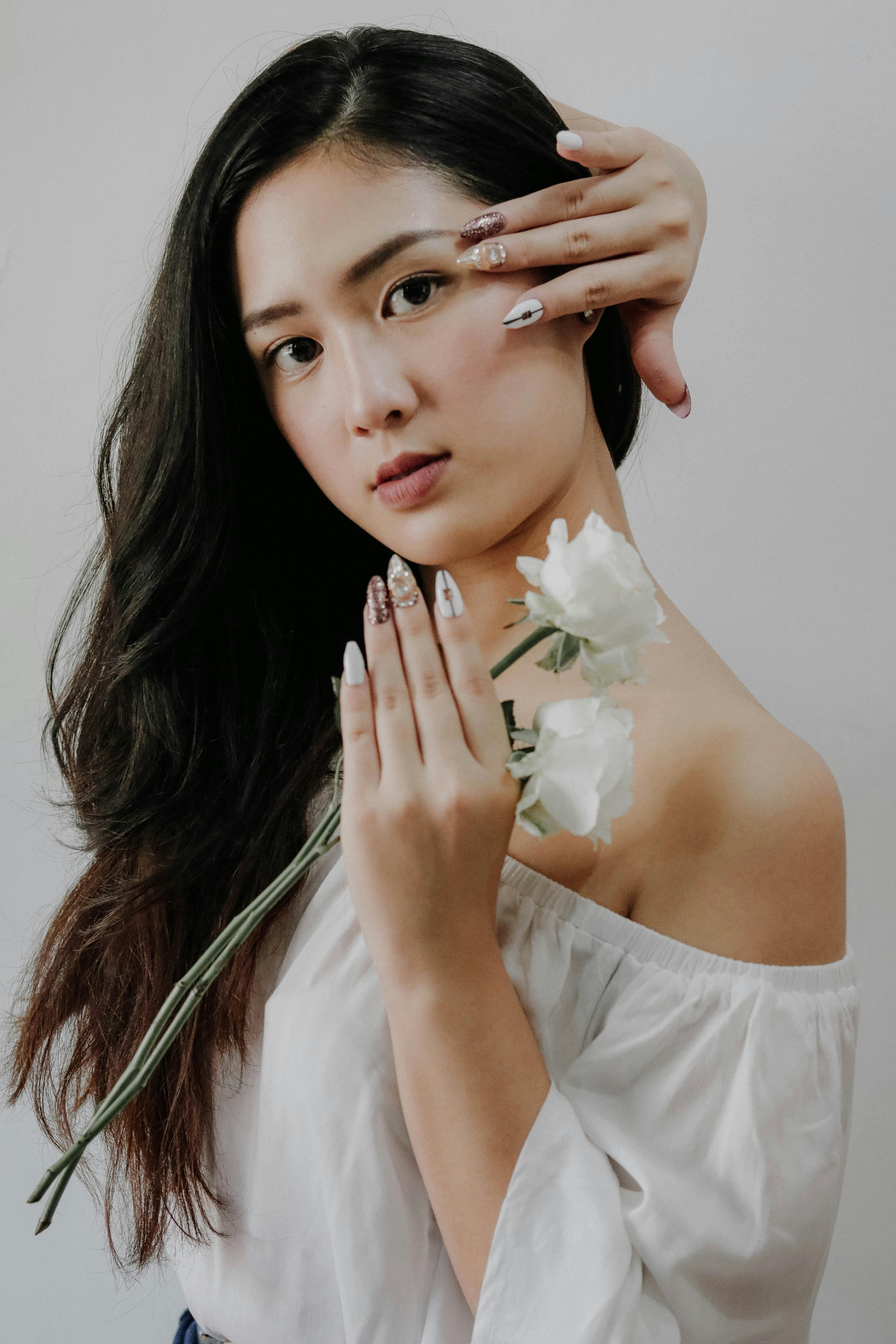 woman wearing white off shoulder blouse holding white rose flower while touching her hair