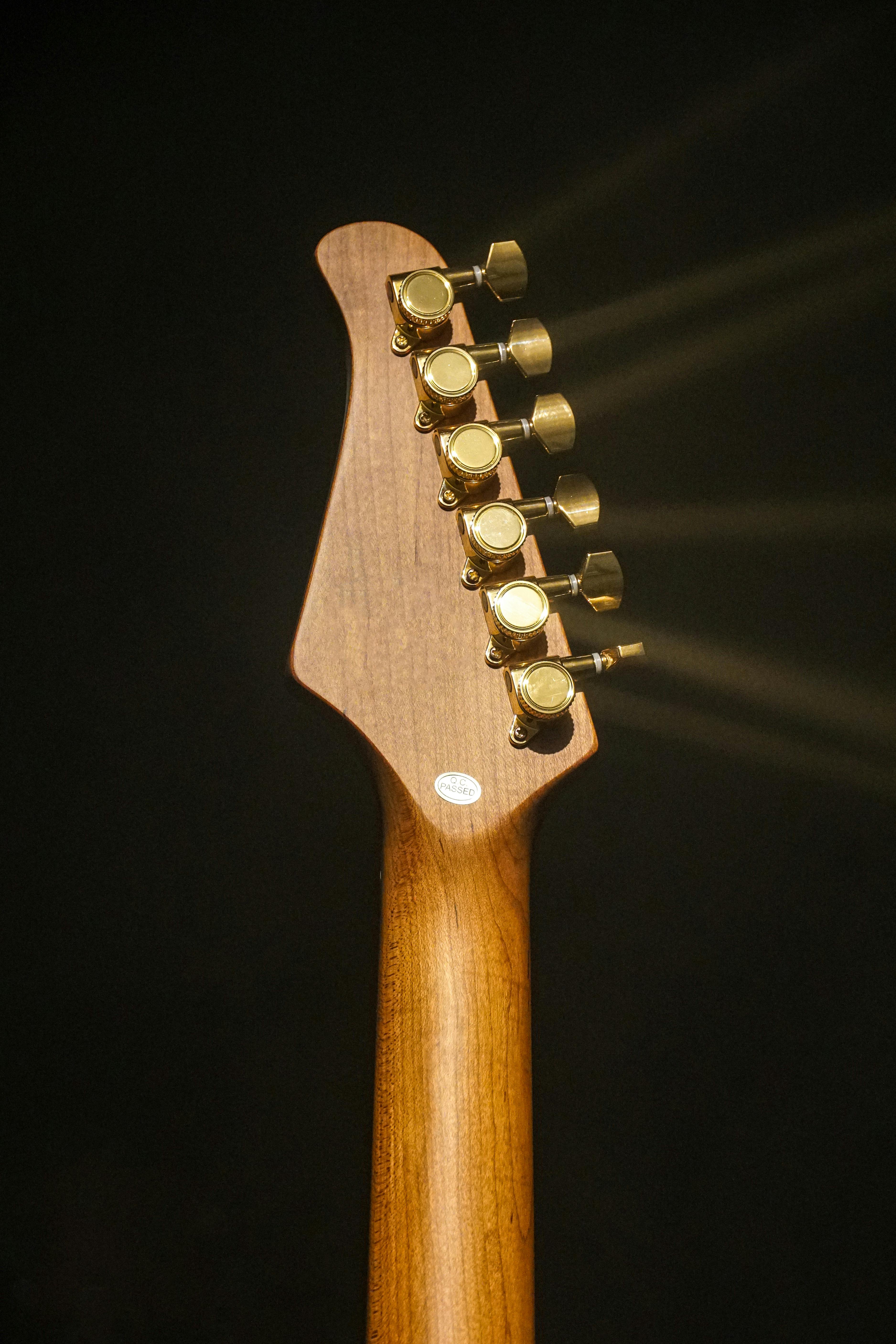 Kostnadsfria Elegant gitarrhuvud i trä med guldfärgade stämskruvar upplysta av en spotlight. Stock foto