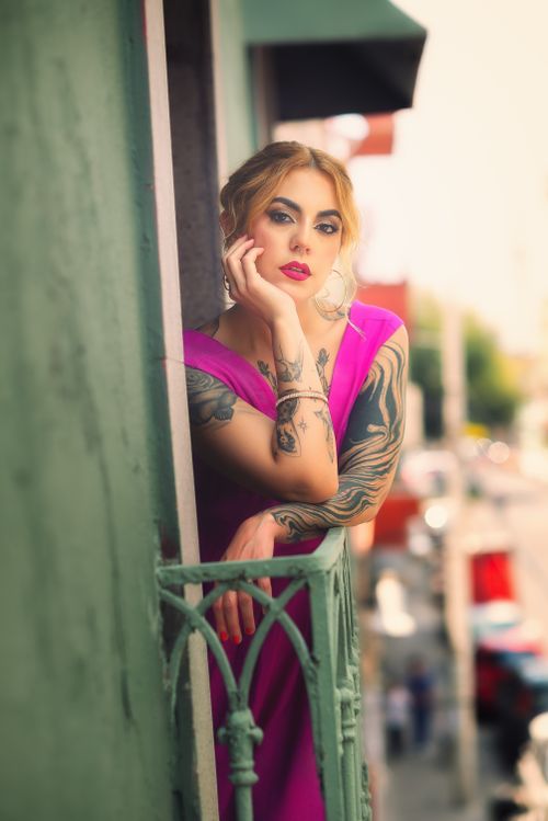 Free Stylish woman with tattoos in pink dress leaning on urban balcony railing, glowing with elegance. Stock Photo