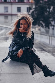 一位时尚女性穿着黑色皮夹克，微笑着坐在户外
