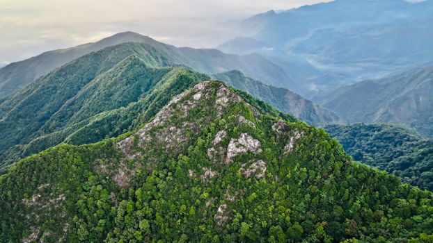 Aerial shot of lush green mountains under cloudy skies, showcasing natural beauty.