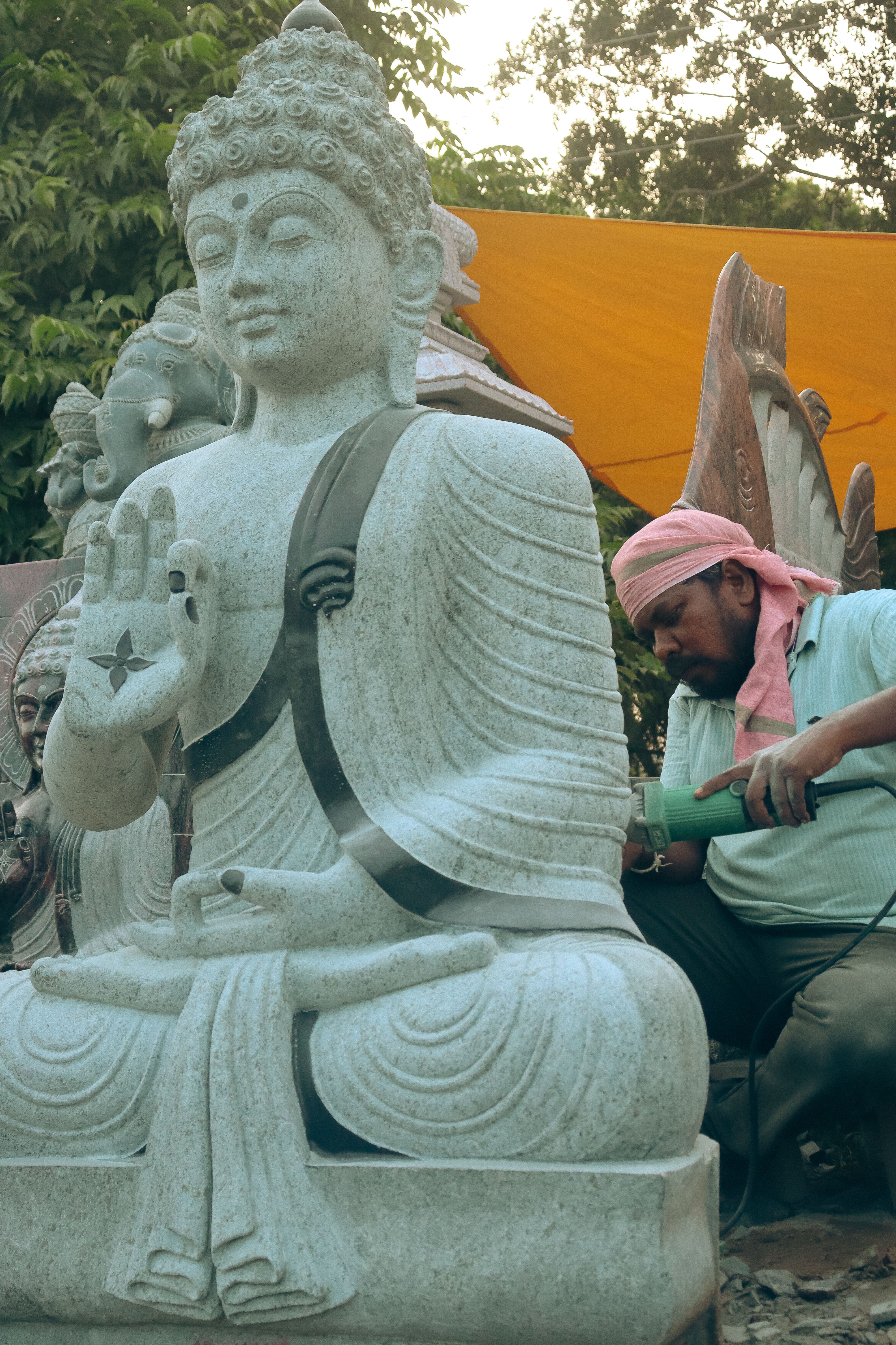 Artisan skillfully carving a stone Buddha statue outdoors, showcasing traditional craftsmanship.