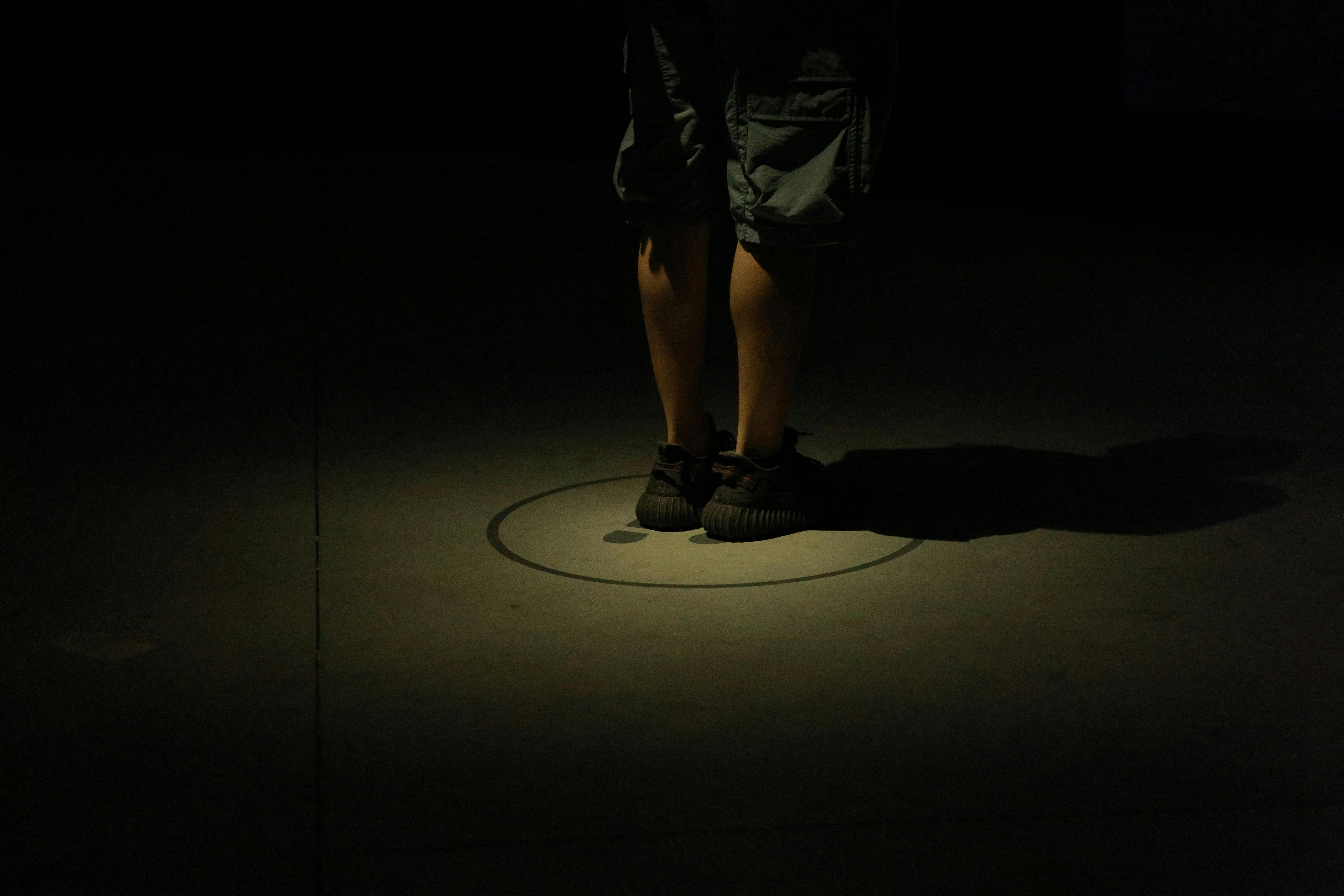 Ücretsiz Karanlık spot ışığı altında bacakların yakın çekimi, gizemli ve dramatik bir atmosfer yaratıyor. Stok Fotoğraflar