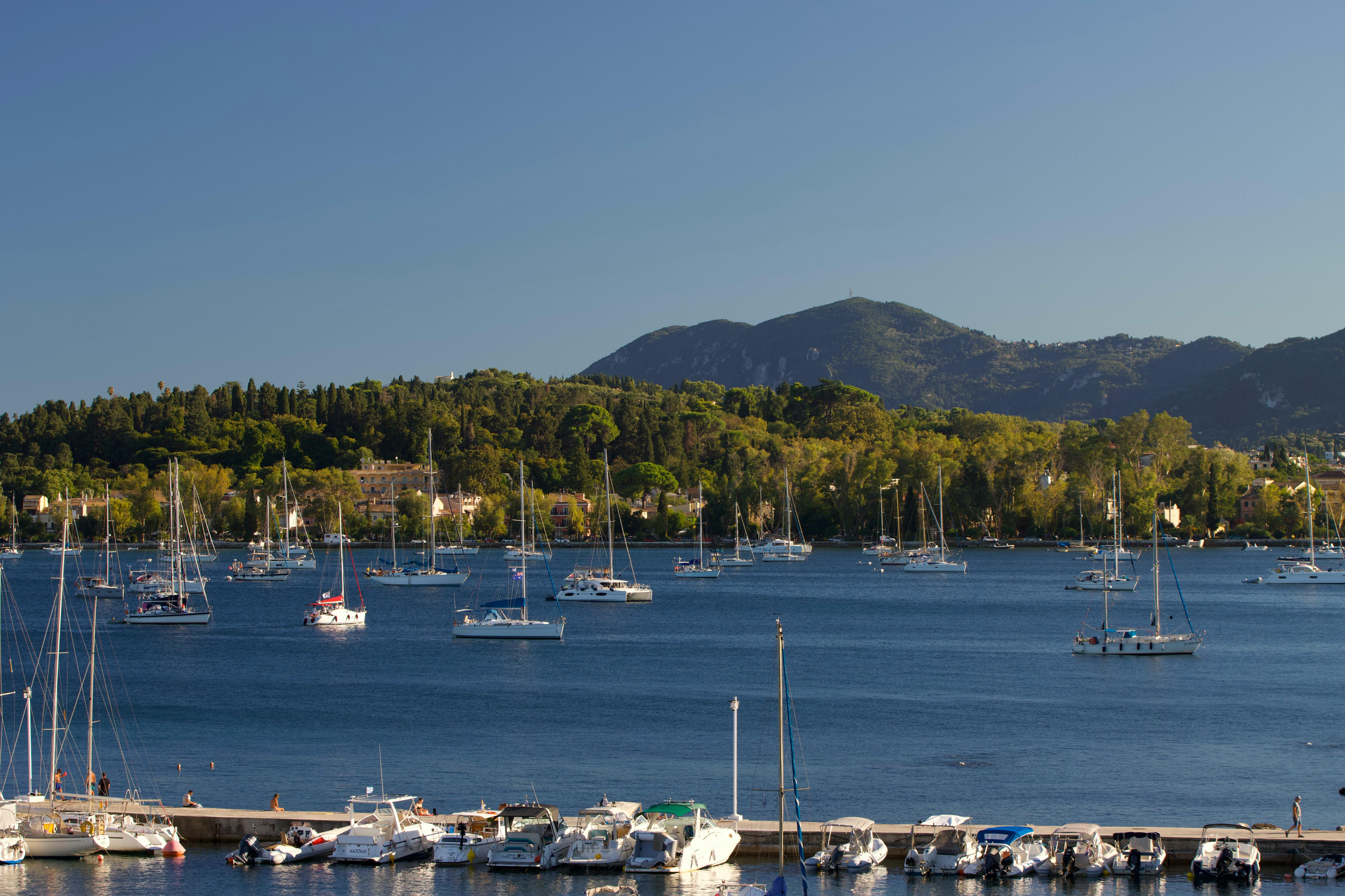 Beautiful panoramic view of boats in the harbor with green hills in Corfu, Greece during summer.