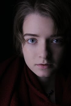A close-up portrait of a young adult with a serious expression and captivating eyes, set against a dark background.