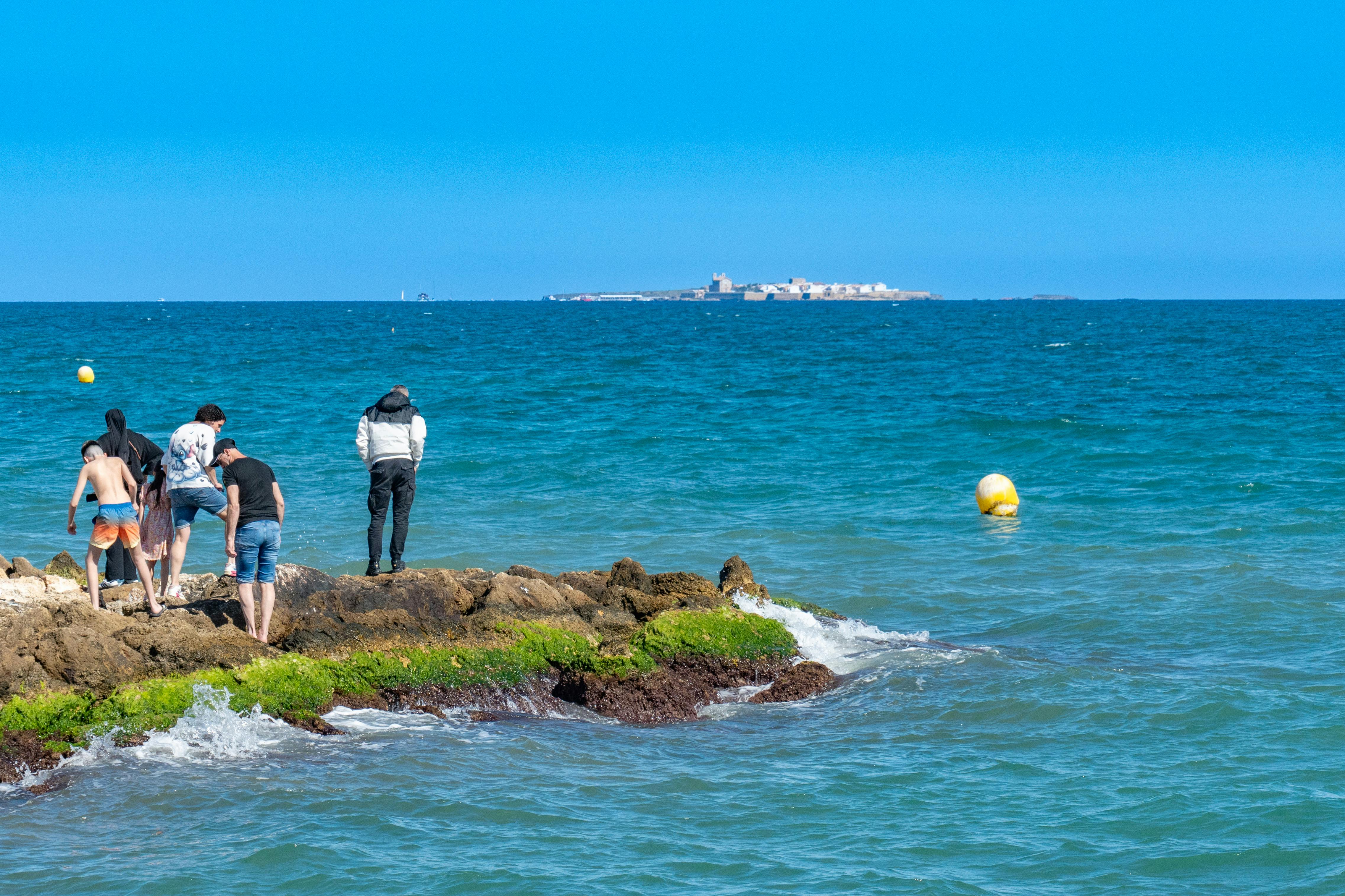 Group of people on rocky shore with a distant island view in Santa Pola, Spain.