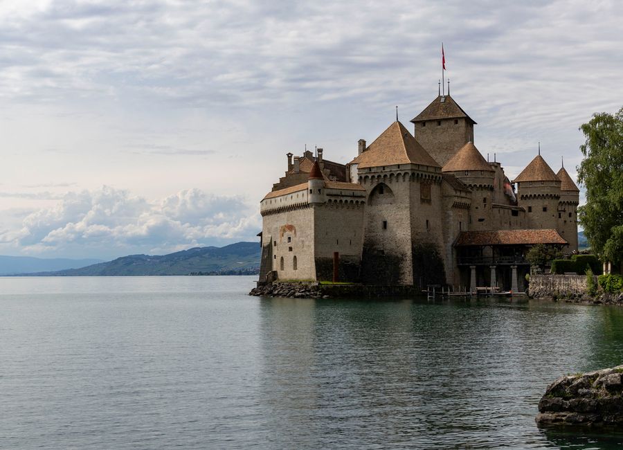 A serene view of Chillon Castle by Lake Geneva with a backdrop of lush hills in Veytaux, Switzerland.