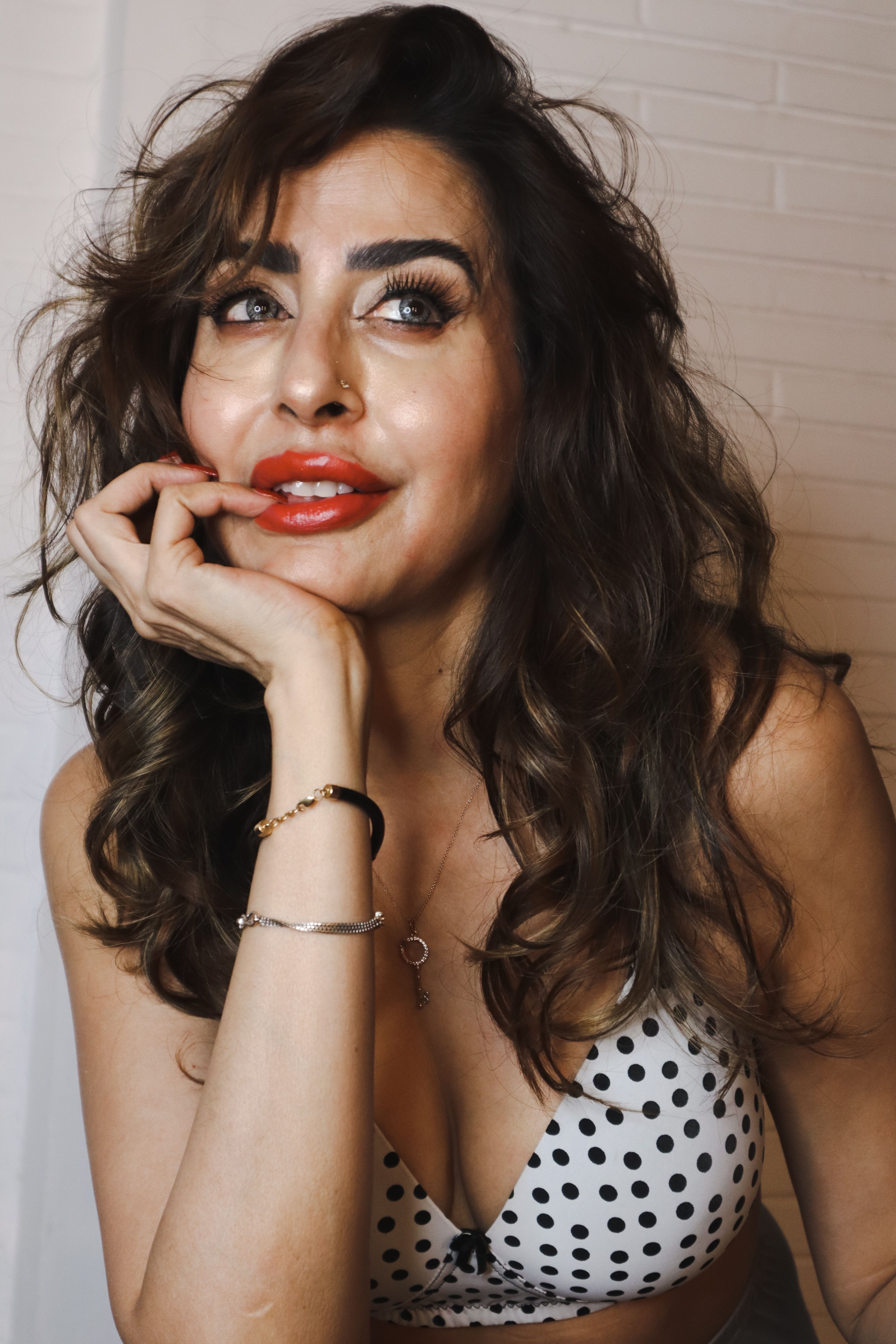 Elegant woman posing with a thoughtful smile wearing a polka dot top.